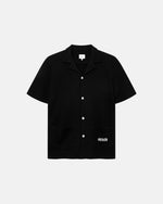 Black waffle-patterned short-sleeved shirt with two front pockets, featuring a stitched black Nikben logo on the left pocket and button closure.