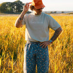 Model standing in a field wearing beige T-shirt  with text on chest and orange cap 