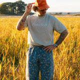 Model standing in a field wearing beige T-shirt  with text on chest and orange cap 