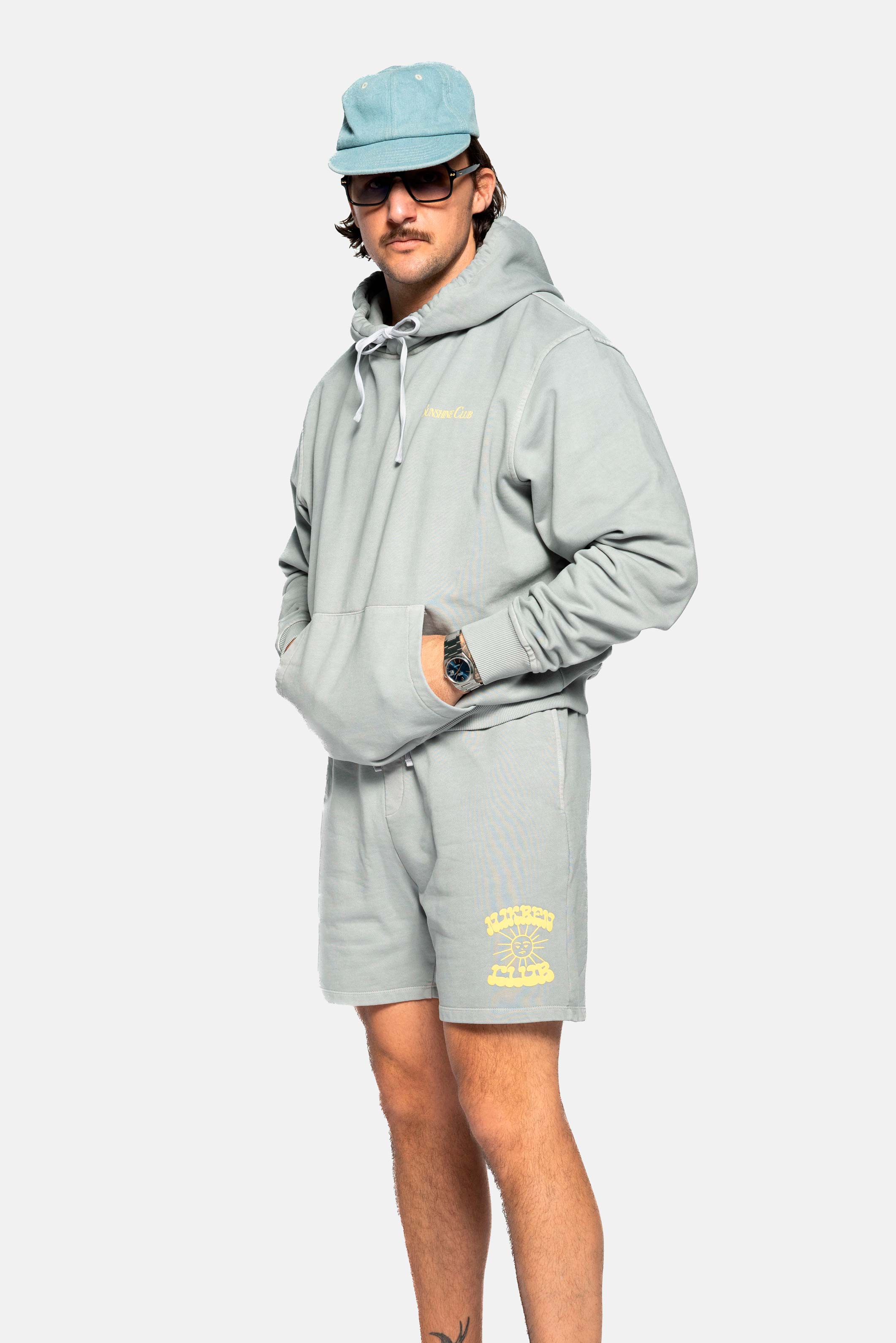 Male model wearing grey hoodie with  drawstrings, chest pocket, ribbed cuffs and yellow Nikben sunshine print