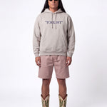 Front of male model wearing grey hoodie with blue "TOURIST" print on the middle chest
