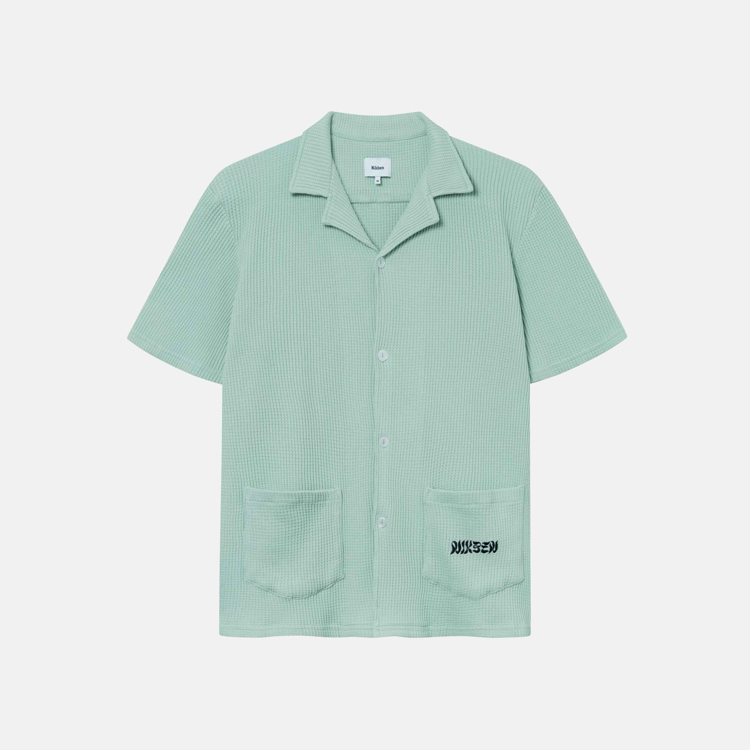 Mint green waffle-patterned short-sleeved shirt with two front pockets, featuring a stitched black Nikben logo on the left pocket and button closure.