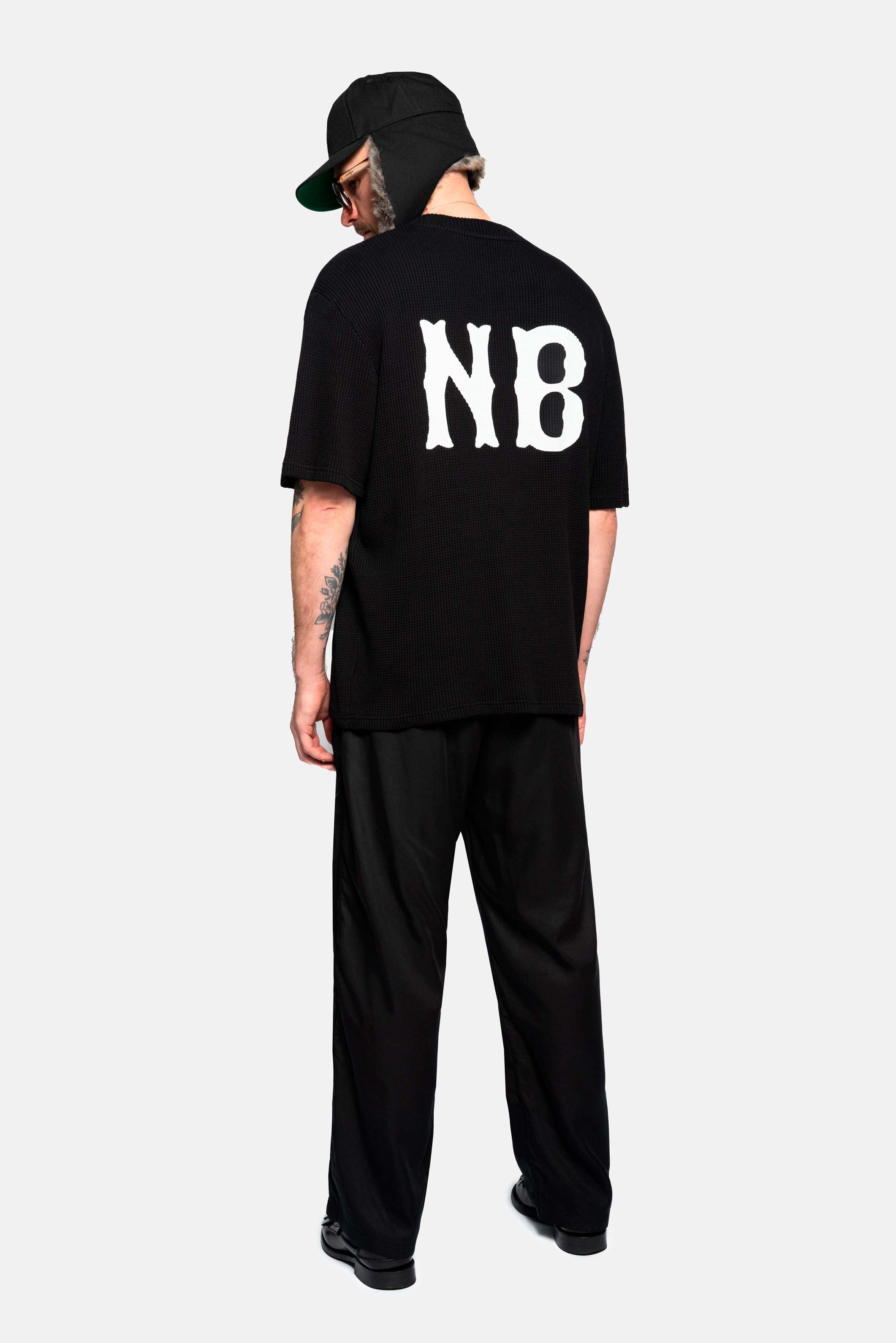 Back of male model wearing a black waffle patterned t-shirt with NB logo print