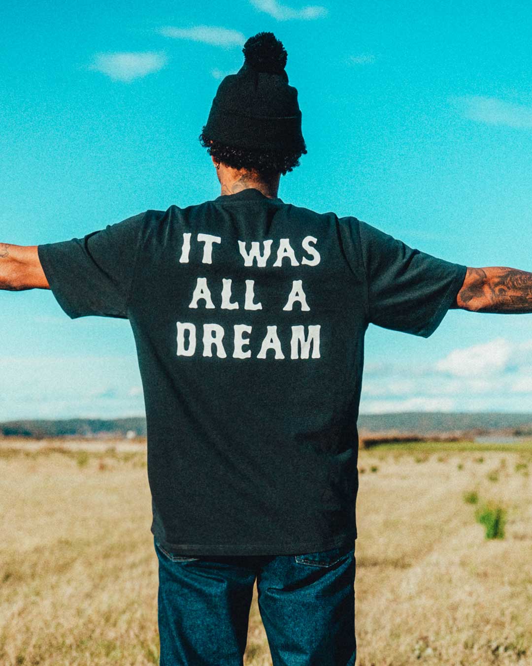 model wearing a black t-shirt with 'IT WAS ALL A DREAM' on the back.