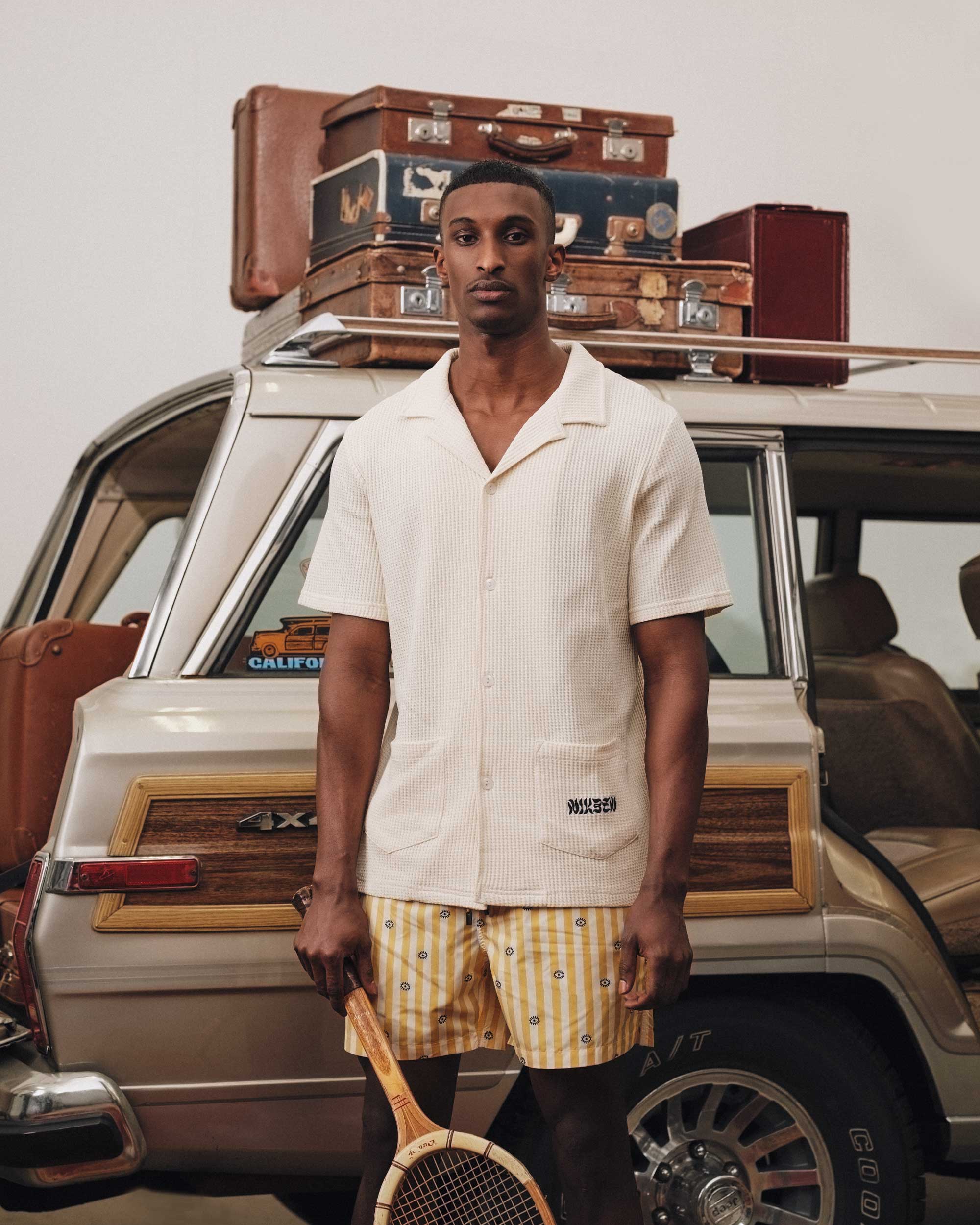 Male model wearing an off white waffle-patterned short-sleeved shirt with two front pockets, featuring a stitched black Nikben logo on the left pocket and button closure.