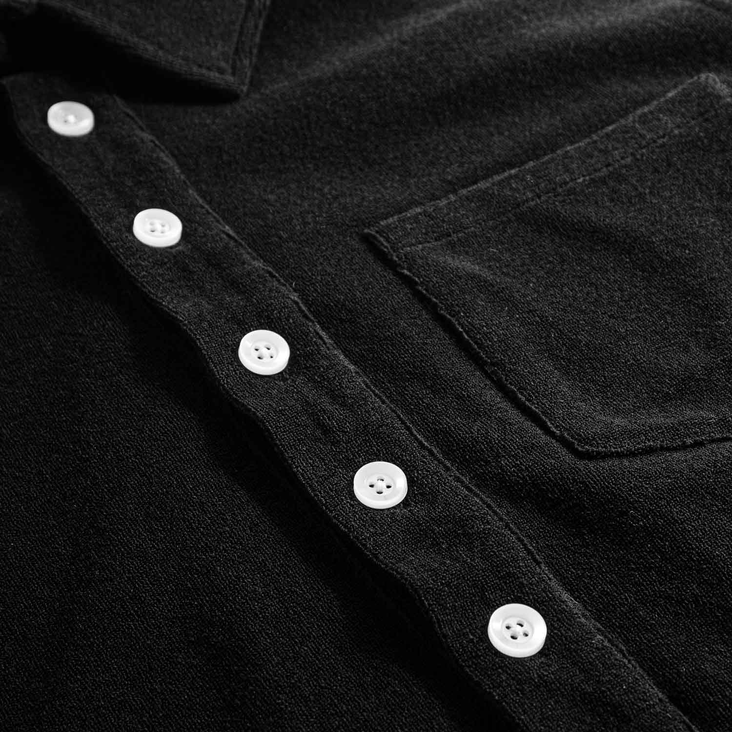 Close up on button closure on a black kaftan in terry toweling fabric.
