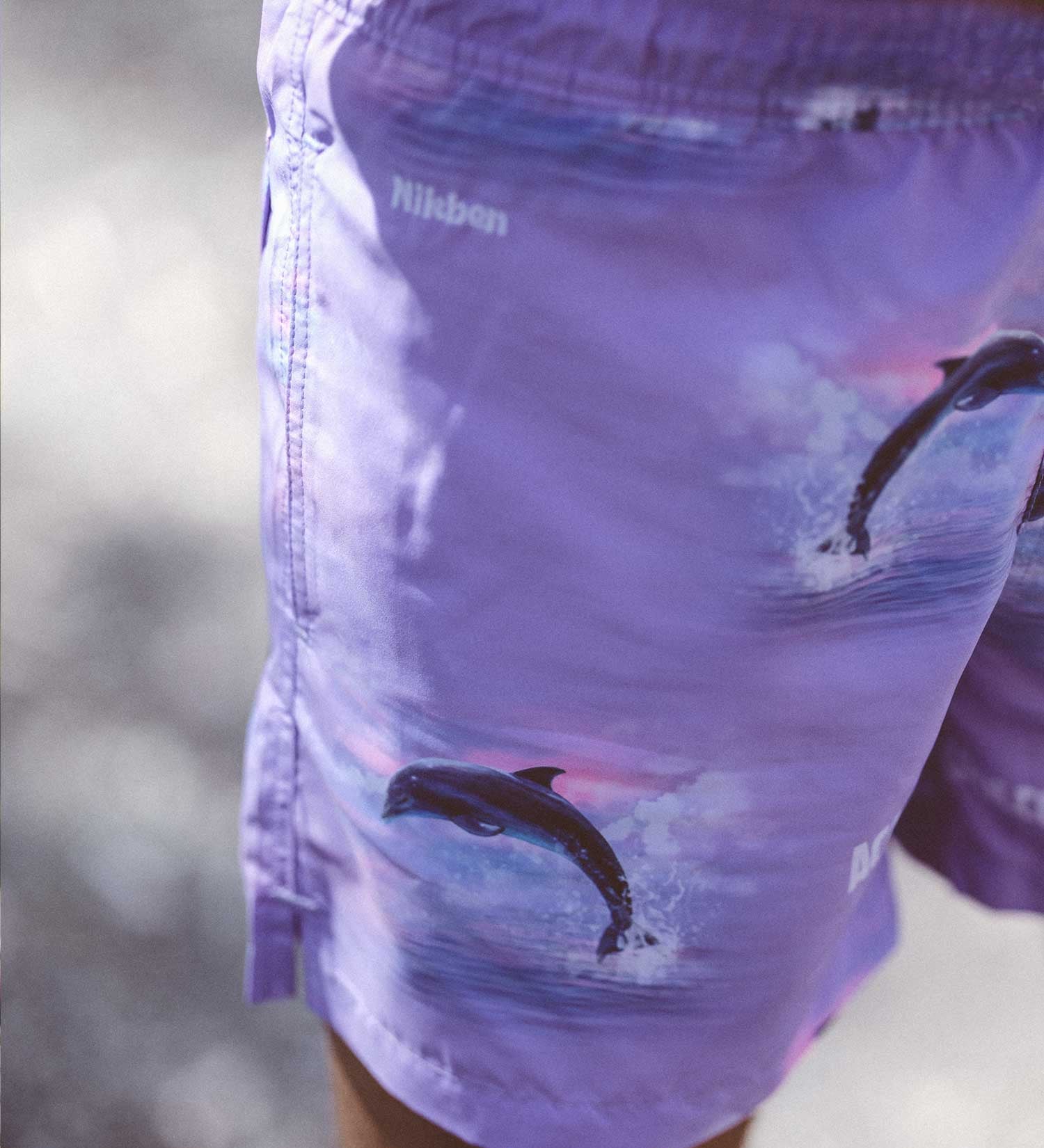 Purple swim trunks with dolphin print and white logo