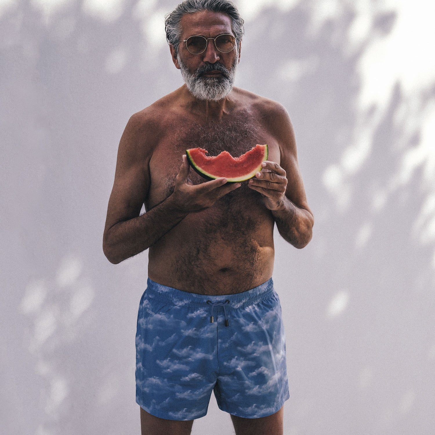 man with blue swim trunks eating watermelon