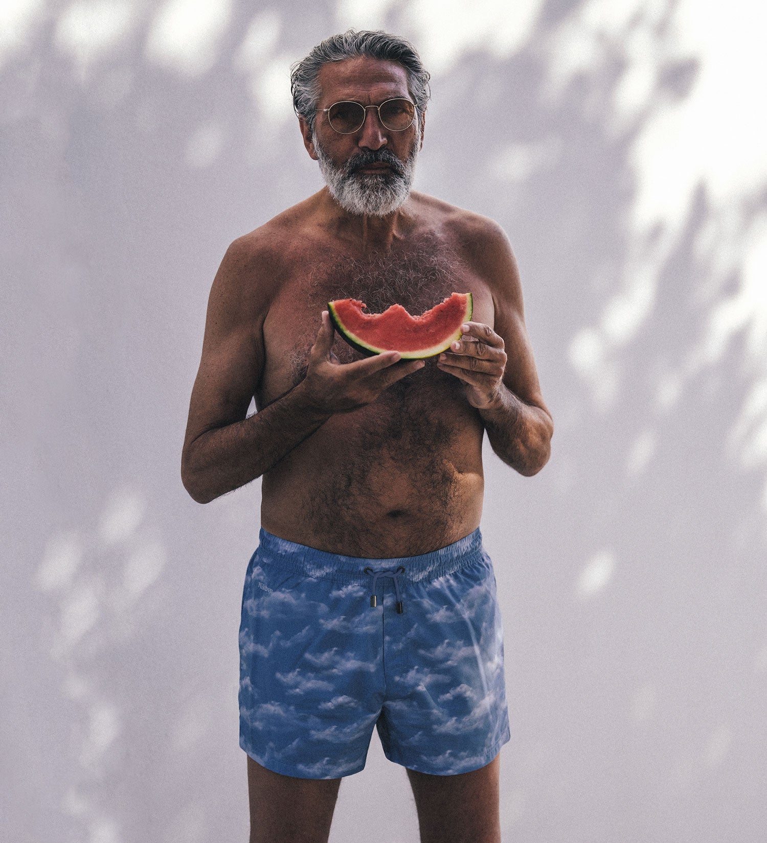 man with blue swim trunks eating watermelon