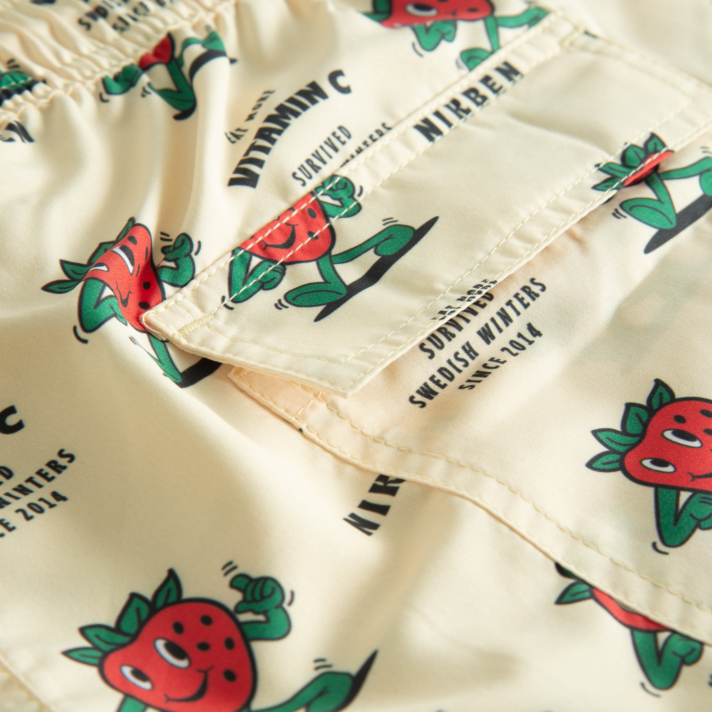 Back pocket on off white swim trunks with strawberries and text