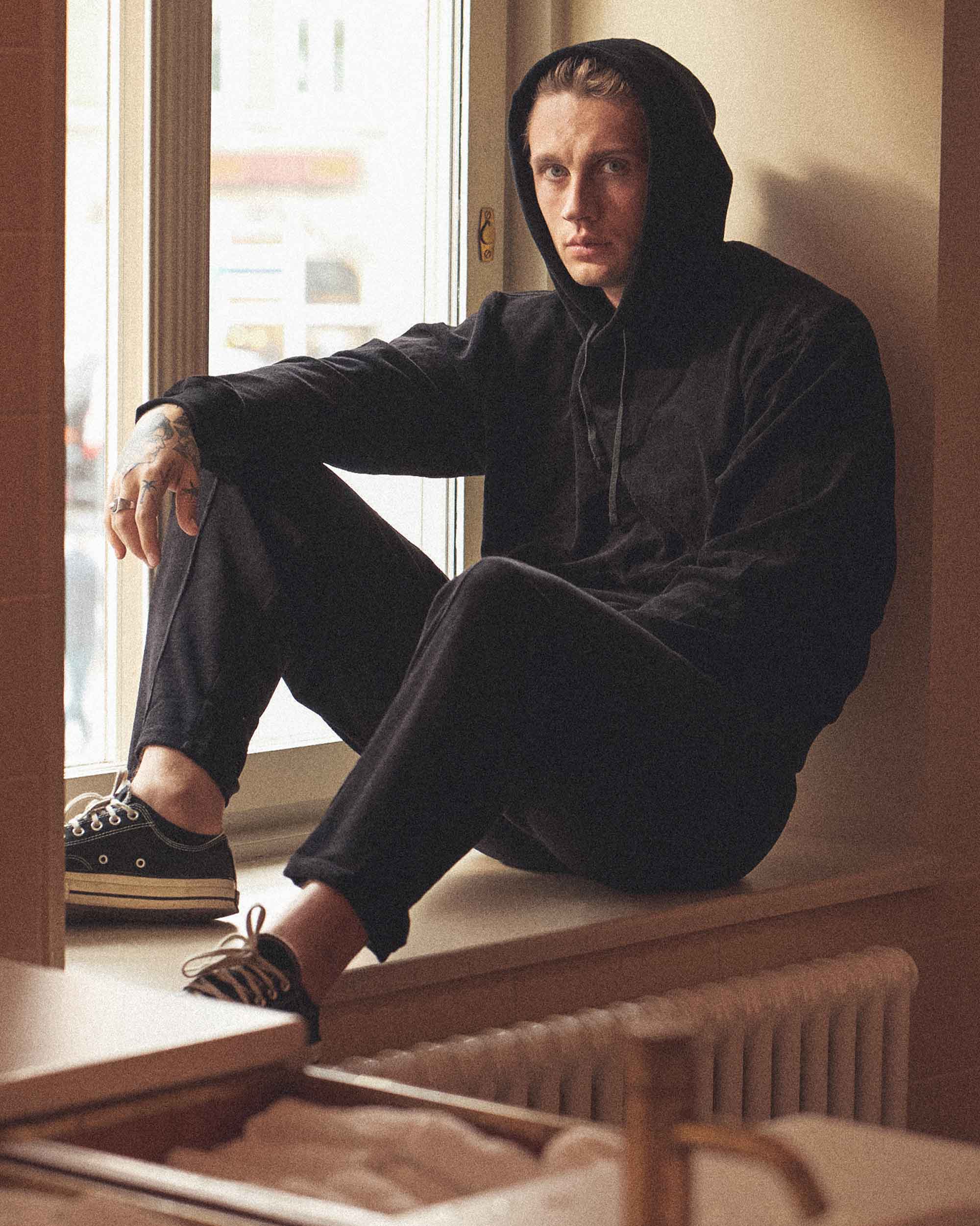 Male model wearing a Female model wearing a black hoodie with drawstrings and a single front pocket.