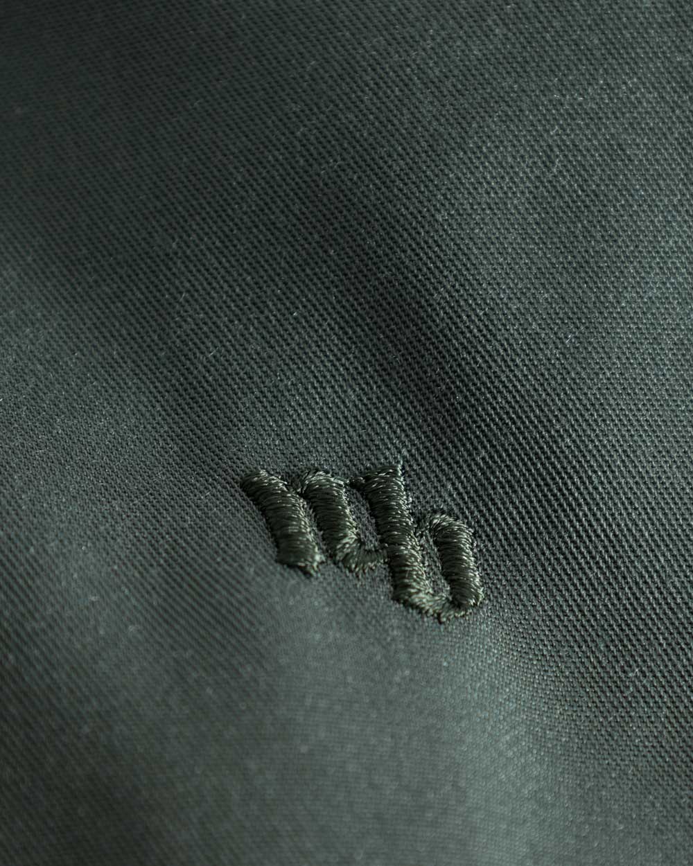 Close up on embroidered logo on green vacation pants with two front pockets and an elastic drawstring.