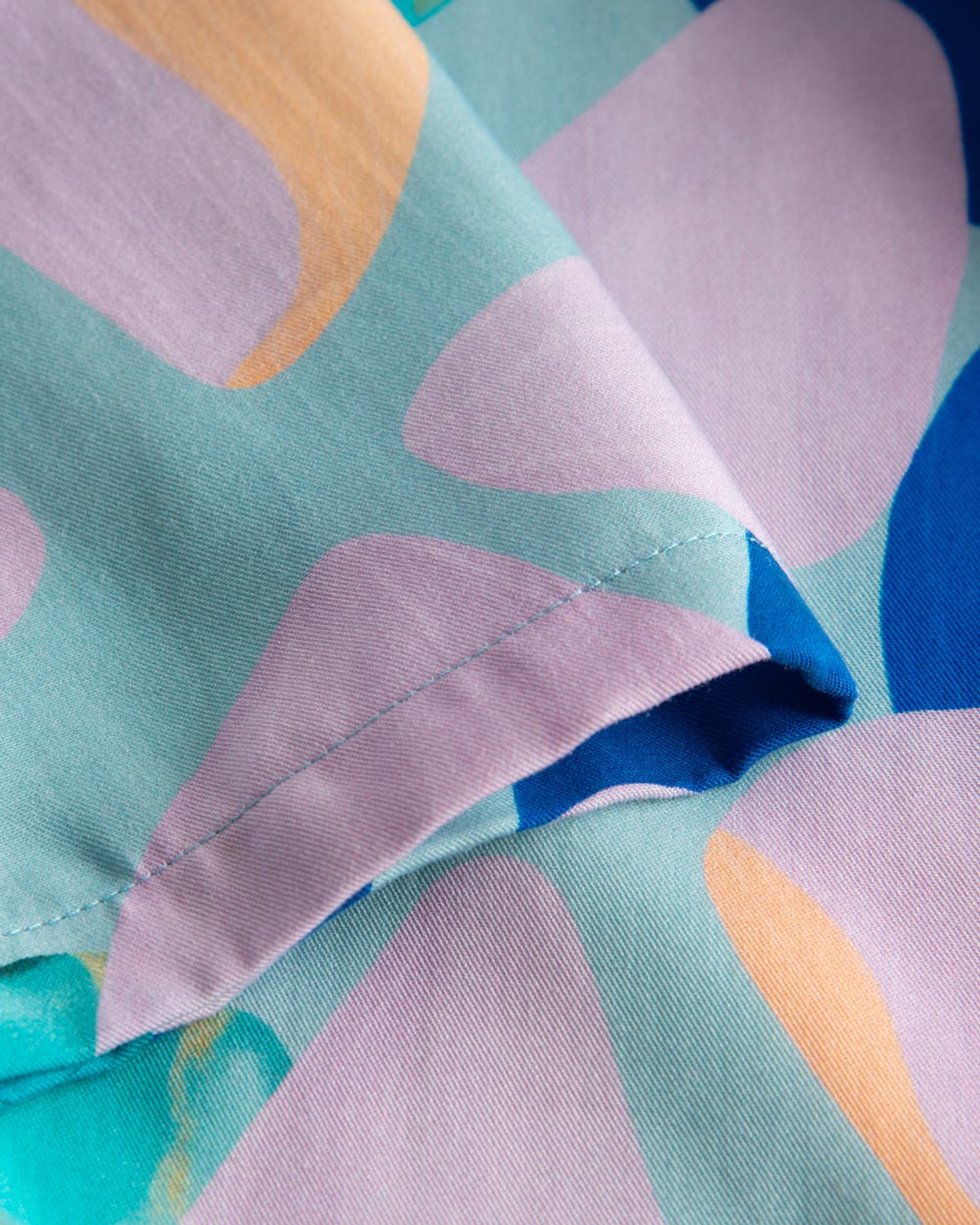 Close up view on stitchings on a short-sleeved vacation shirt with a multi-colored graphic patter