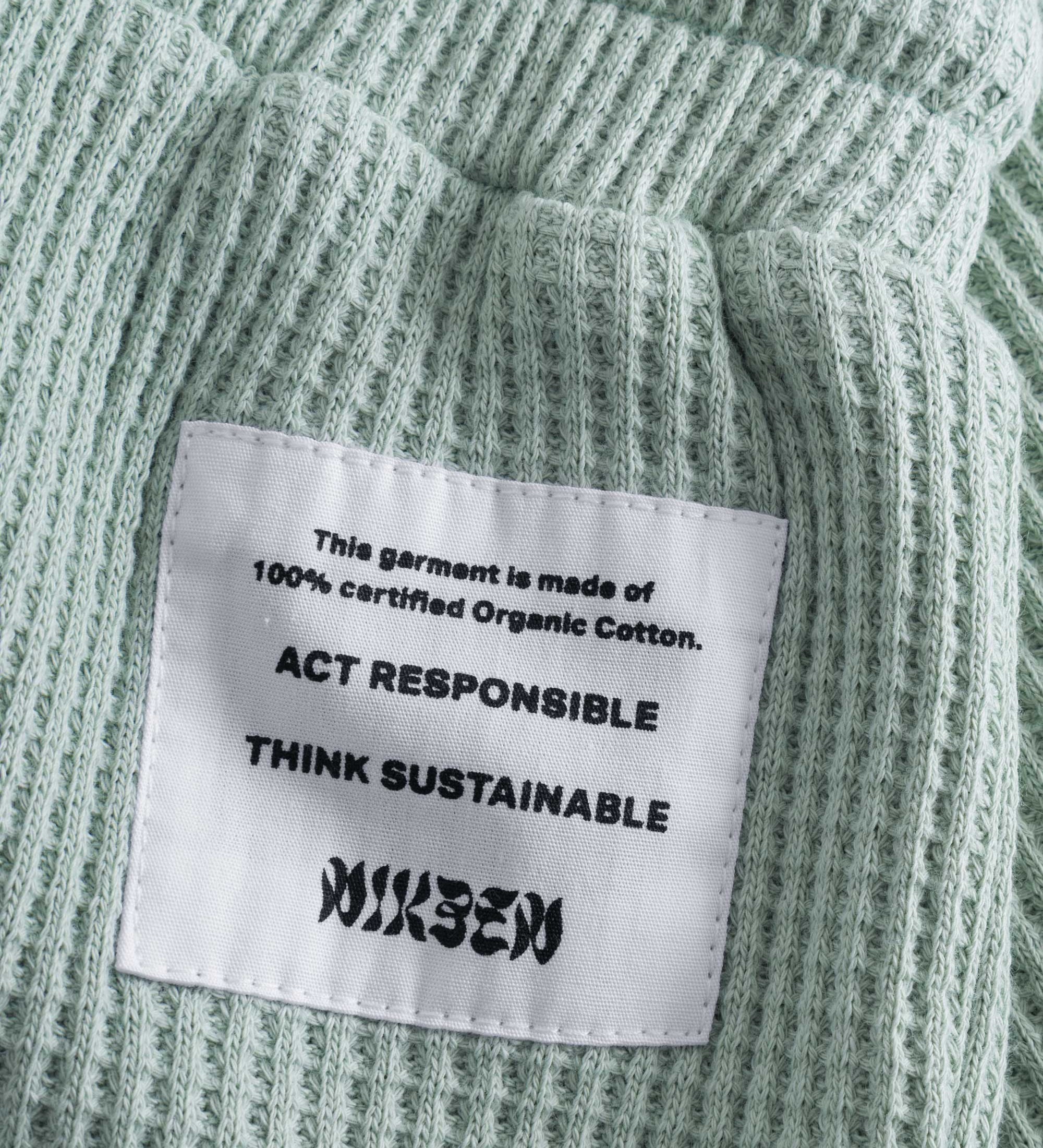 Close up of stitched on material label on mint green waffle-patterned short-length shorts.