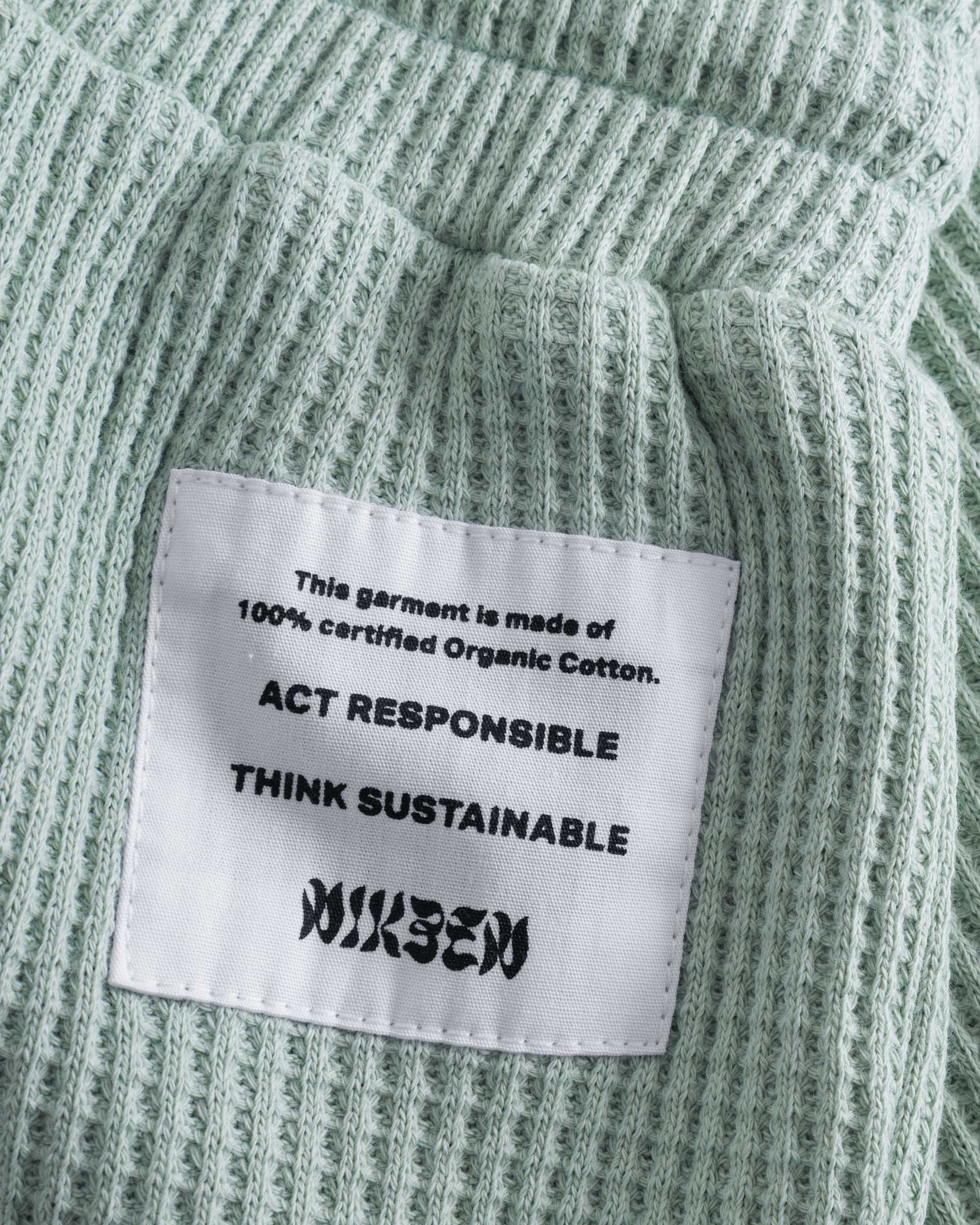 Close up of stitched on material label on mint green waffle-patterned short-length shorts.