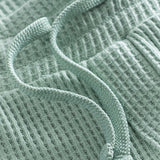 Close up of drawstring on mint green waffle-patterned mid-length shorts.