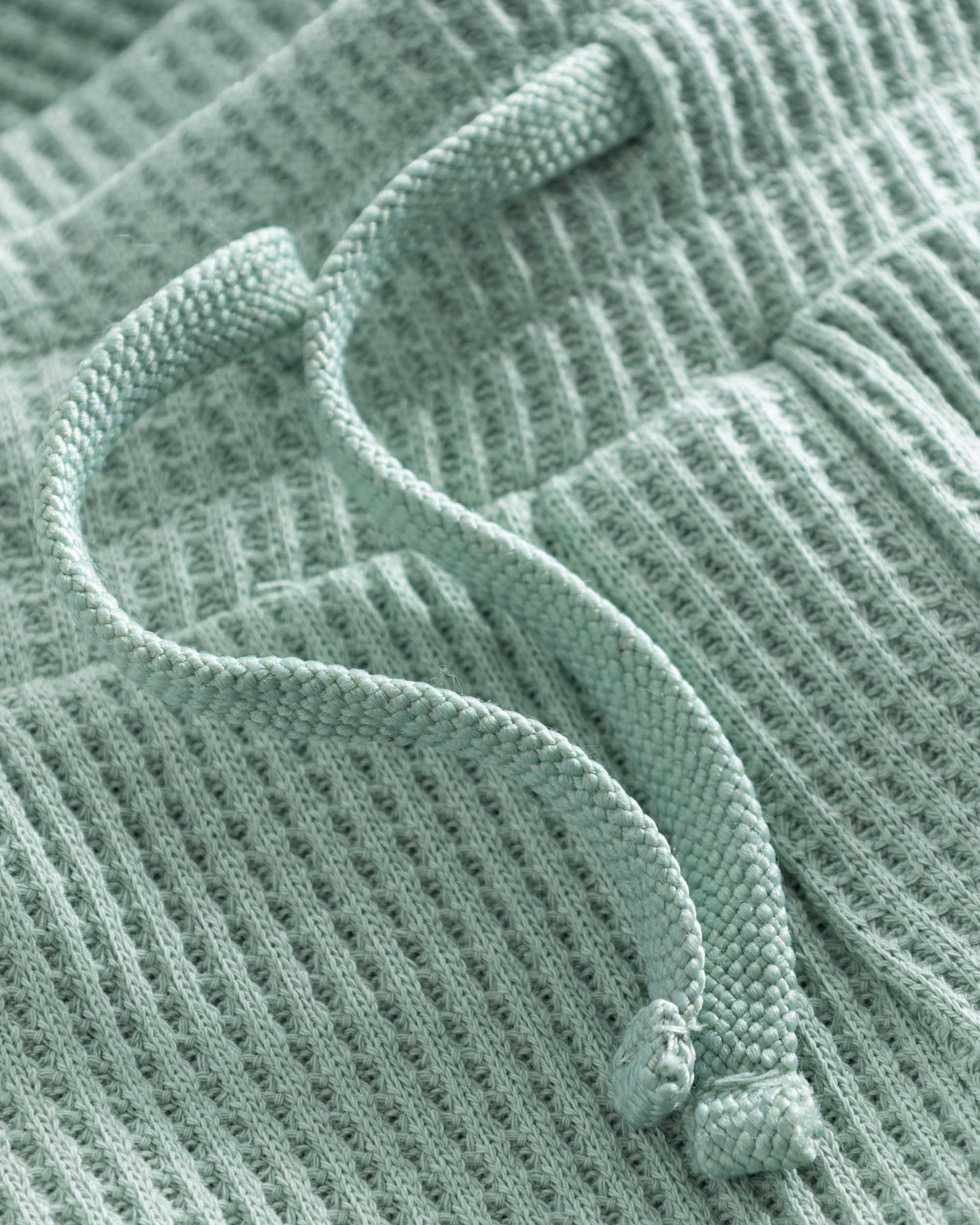 Close up of drawstring on mint green waffle-patterned mid-length shorts.