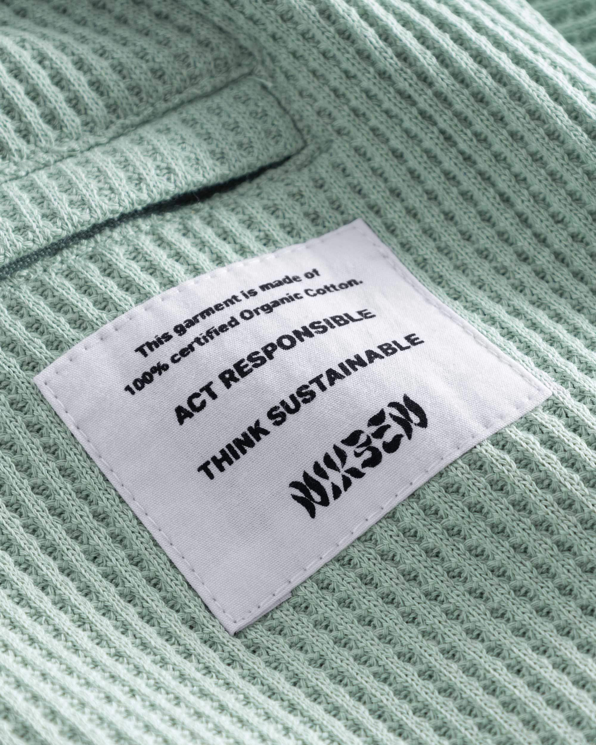 Close up of back pocket and stitched on material label on mint green waffle-patterned mid-length shorts.