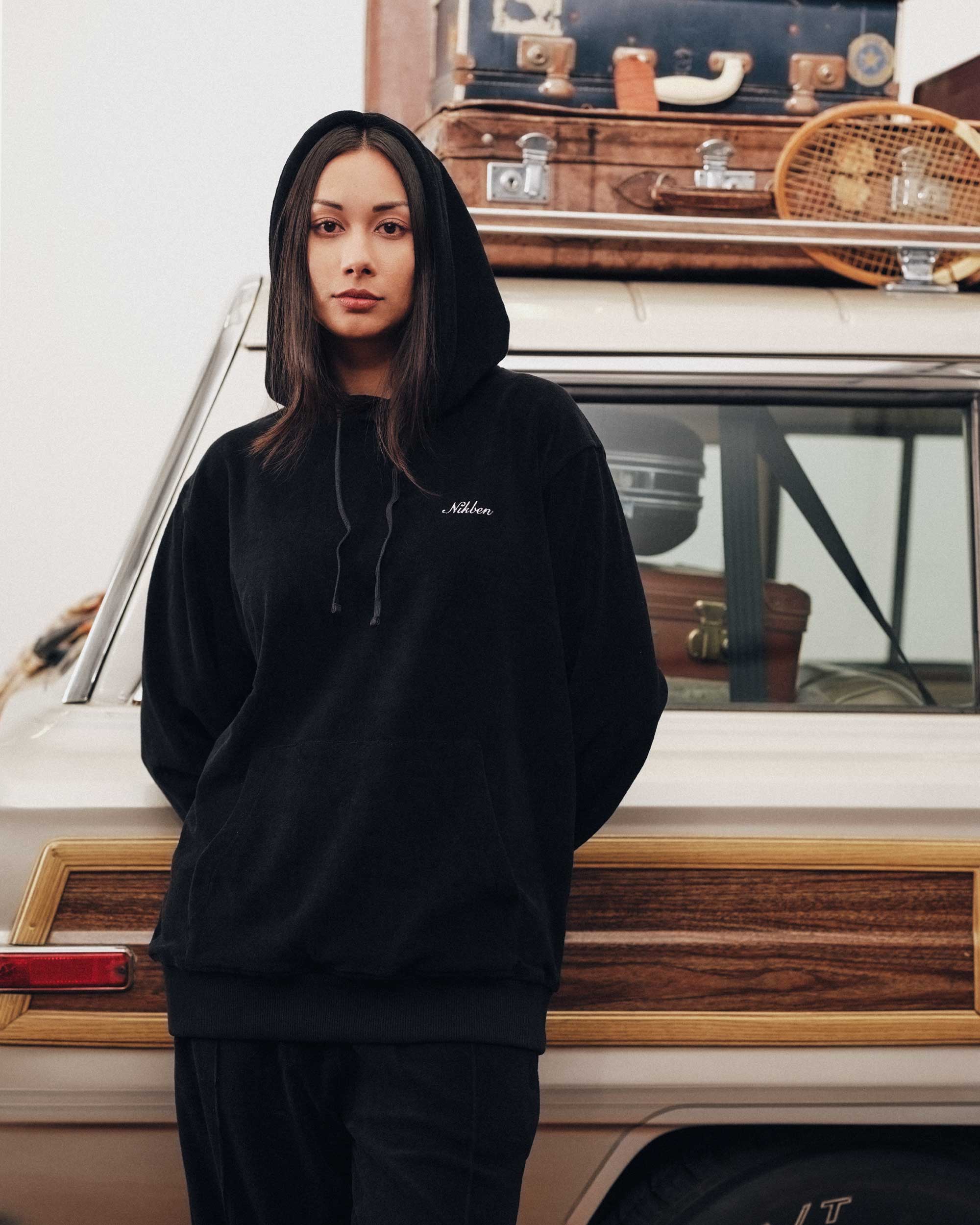 Female model wearing a black hoodie with drawstrings, a single front pocket, and a white "Nikben" logo on the chest.