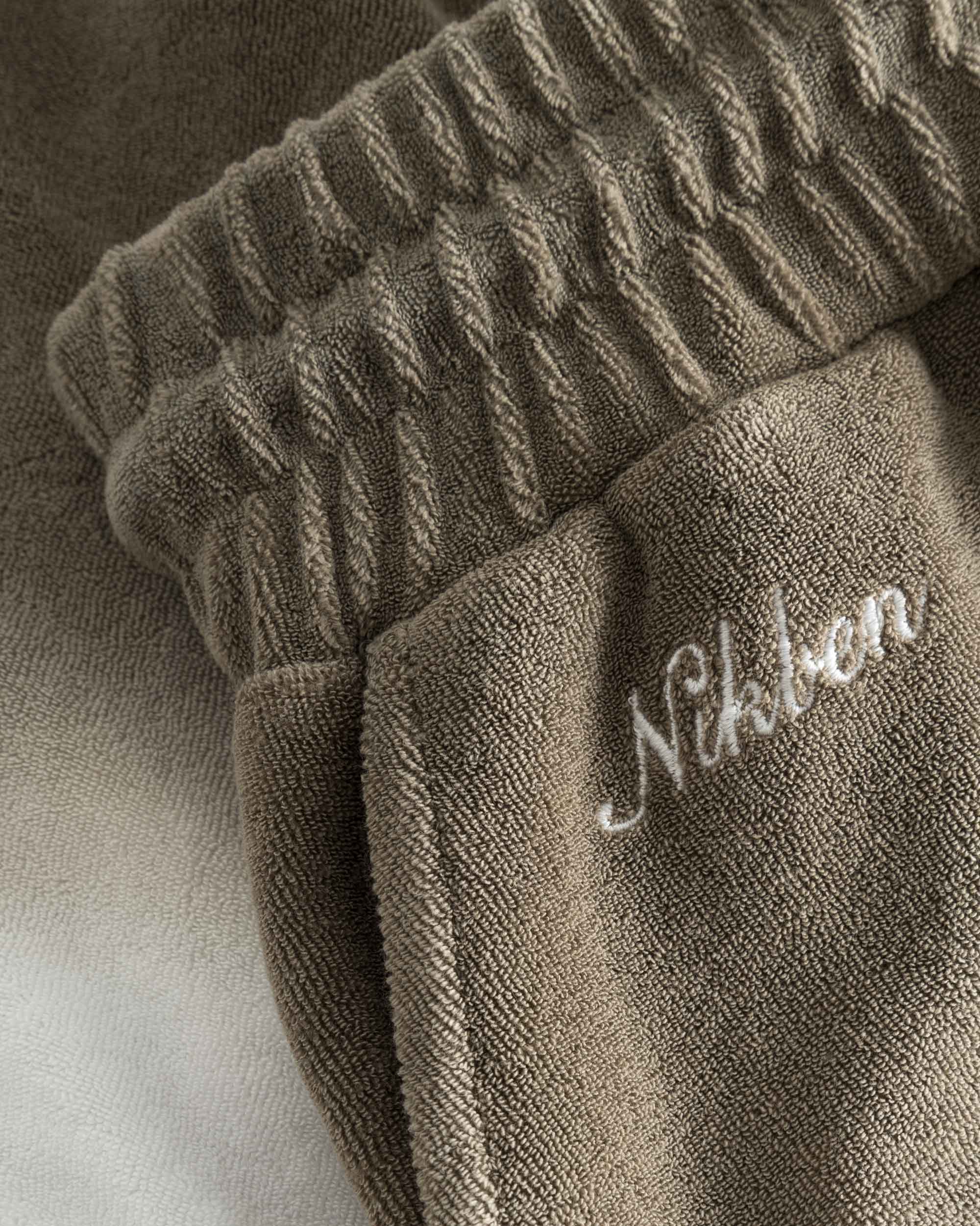 Close up on embroidered logo on brown and white low cut shorts in terry toweling fabric