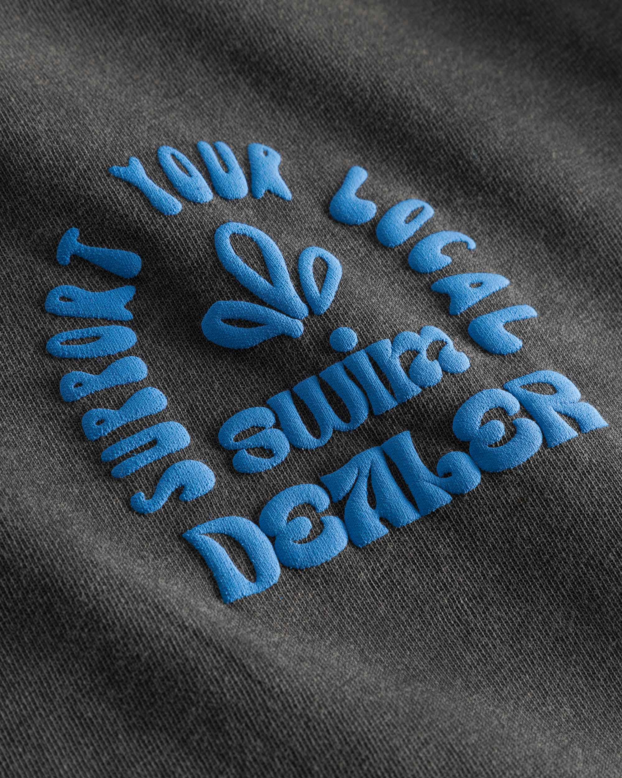 Close up of blue puffy text print on washed black t-shirt.