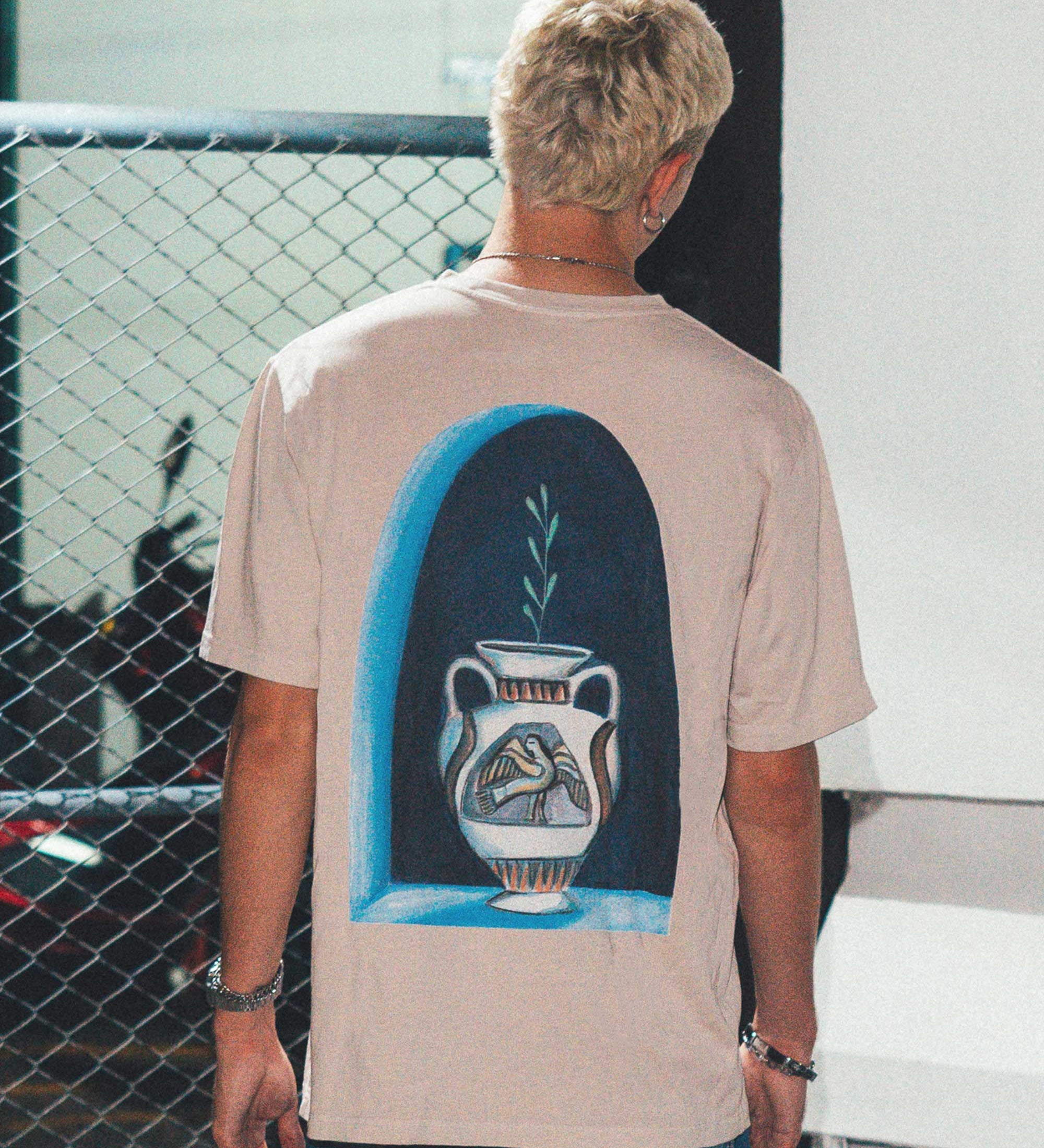 Back view of male model wearing a cream colored t-shirt with a blue vase print.
