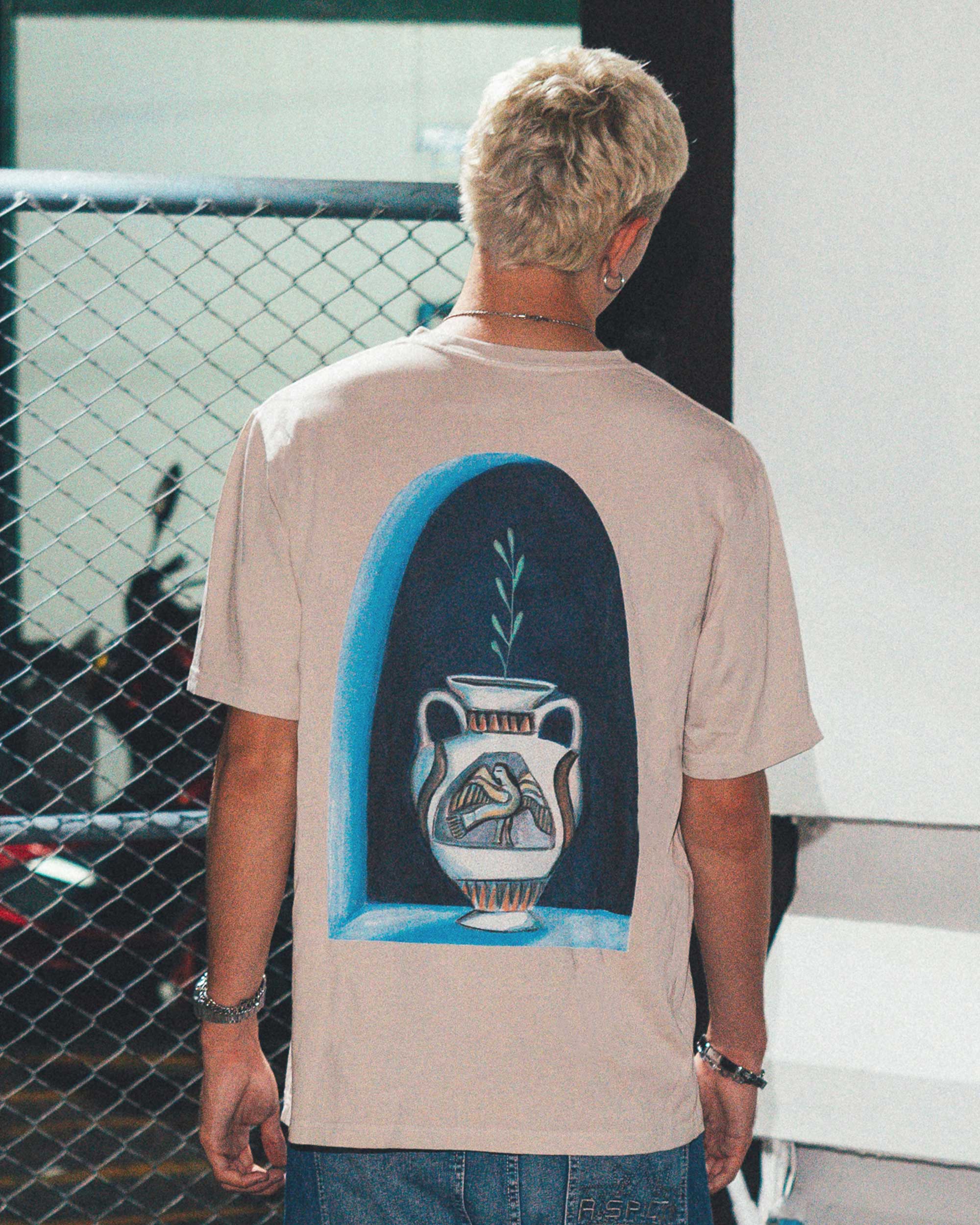 Back view of male model wearing a cream colored t-shirt with a blue vase print.
