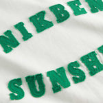 Close up view of "Nikben Sunshine" text on white t-shirt.