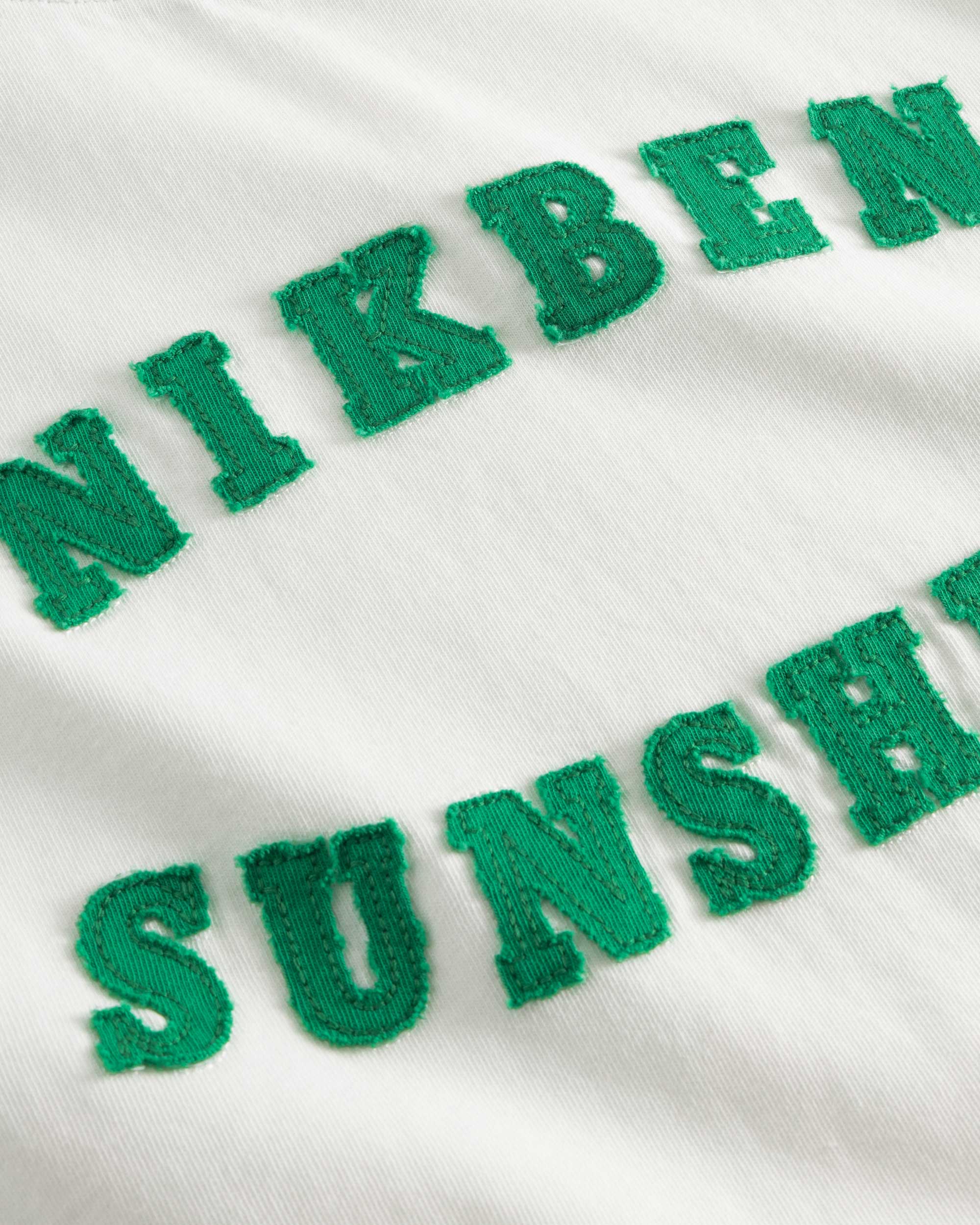 Close up view of "Nikben Sunshine" text on white t-shirt.