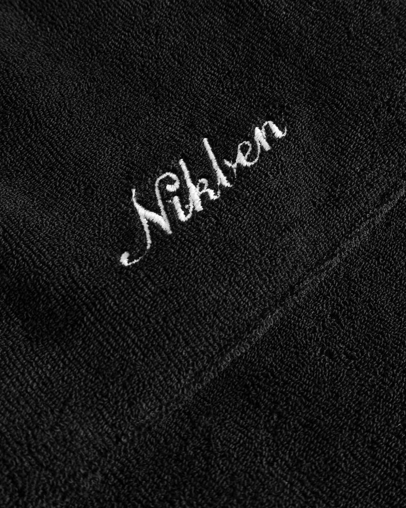 Close up of white embroidered logo on the back of a black short sleeve shirt.