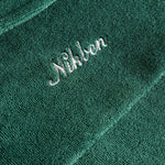 Close up of white embroidered logo on the back of a green short sleeve shirt.