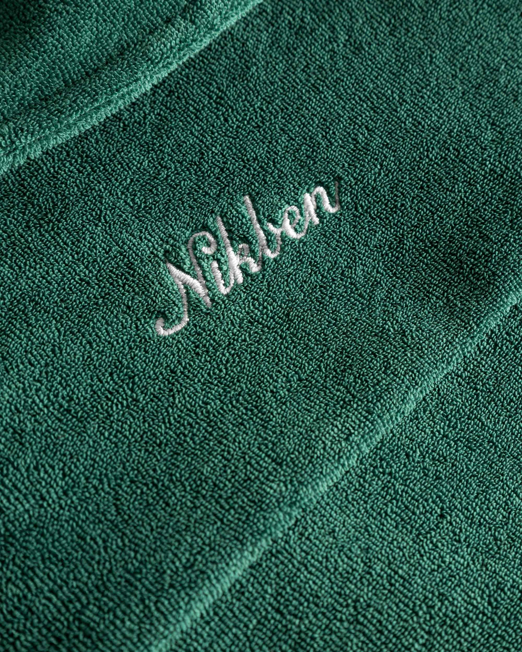 Close up of white embroidered logo on the back of a green short sleeve shirt.