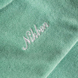 Close up of white embroidered logo on the back of a grey-green short sleeve shirt.