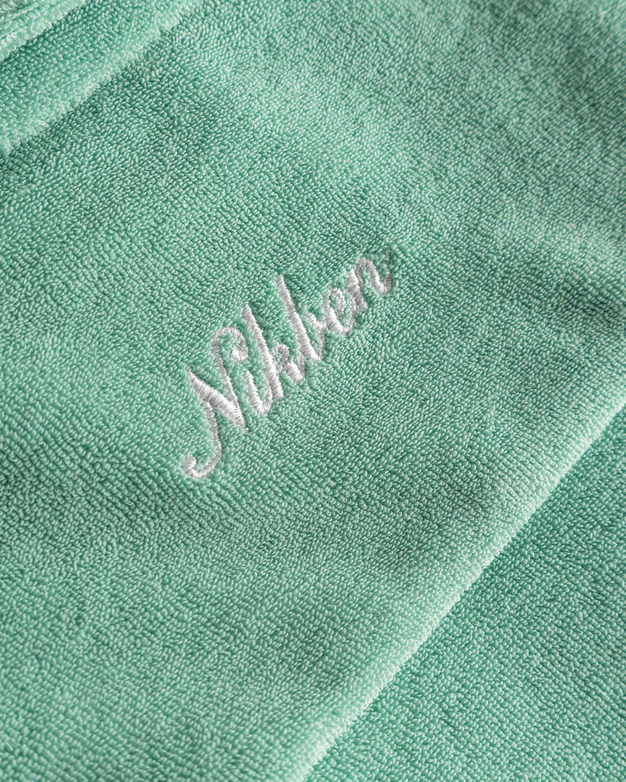 Close up of white embroidered logo on the back of a grey-green short sleeve shirt.