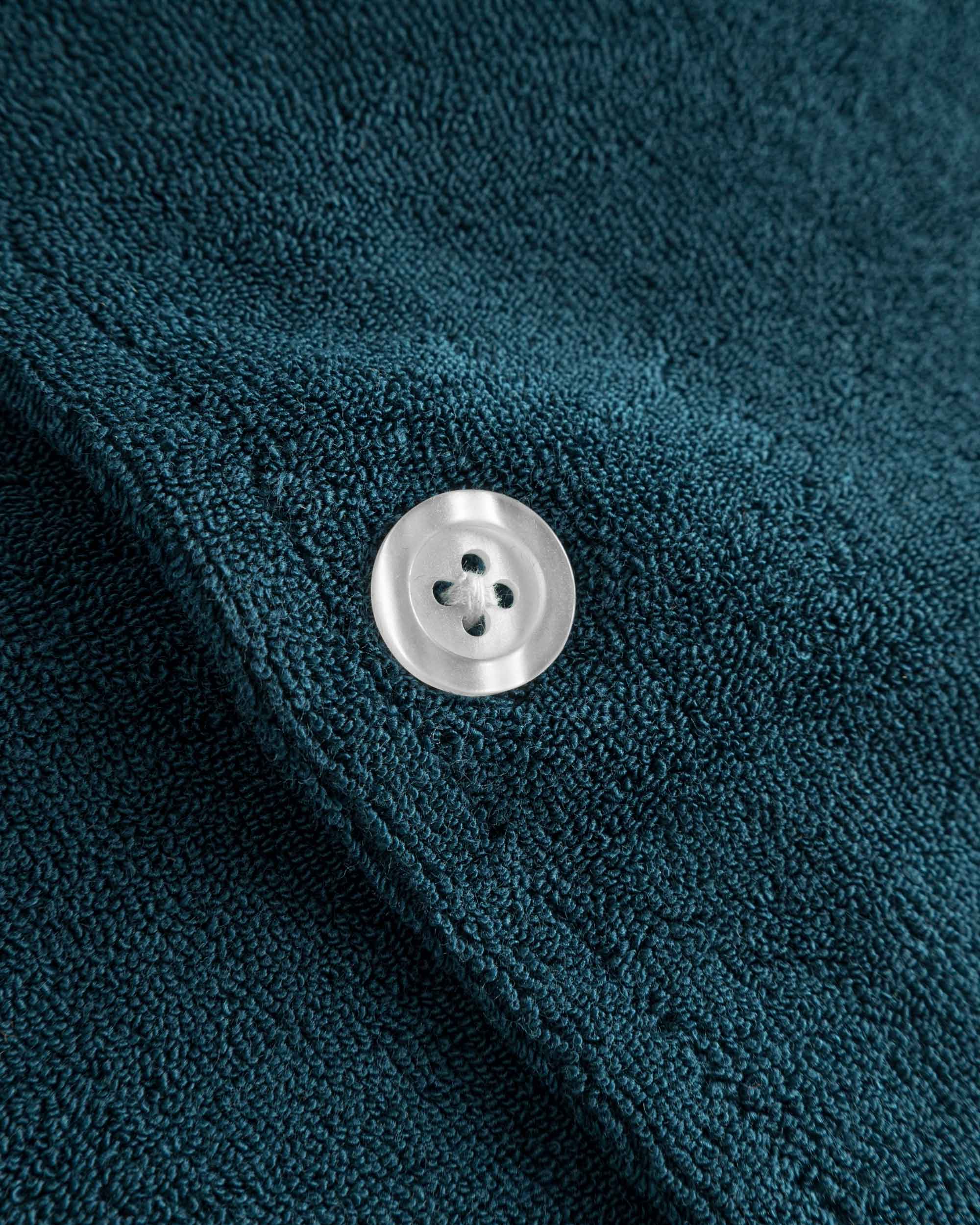 Close up of white pearl button on a navy blue short sleeve shirt.