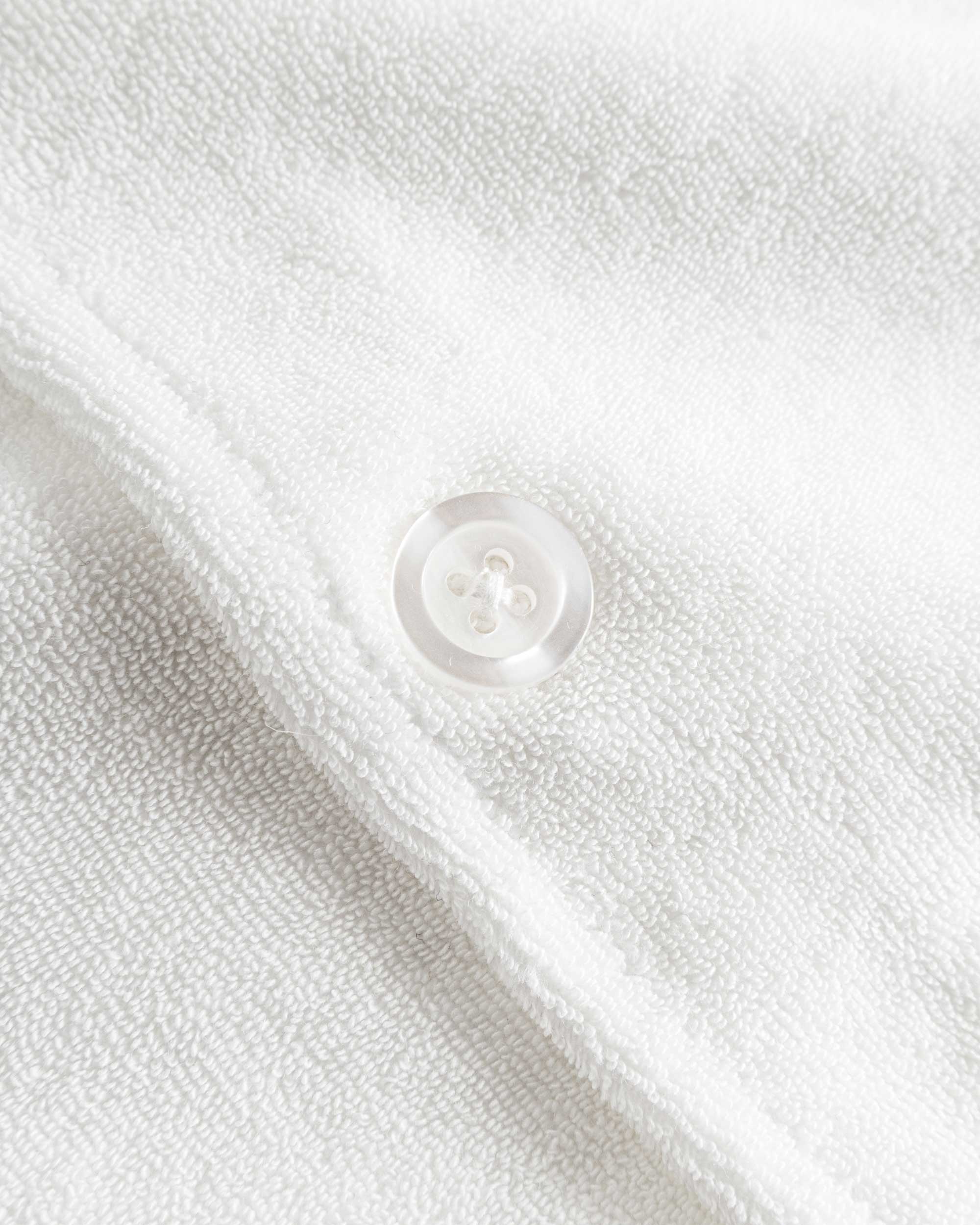 Close up of white pearl button on an off white short sleeve shirt.