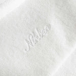 Close up of white embroidered logo on the back of an off white short sleeve shirt.