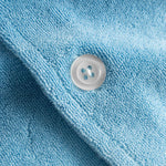 Close up of white pearl button on a white and sky blue short sleeve shirt.