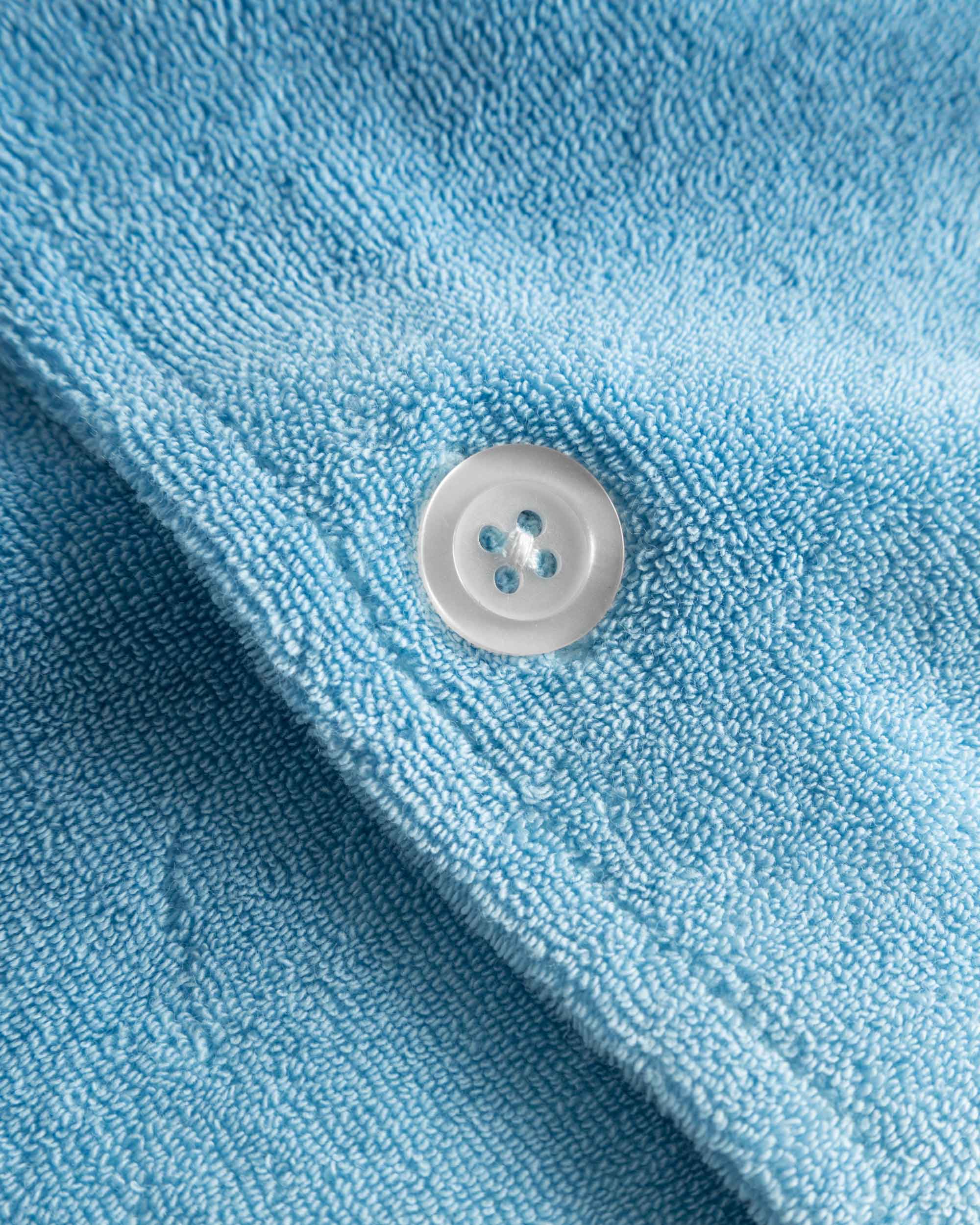 Close up of white pearl button on a white and sky blue short sleeve shirt.