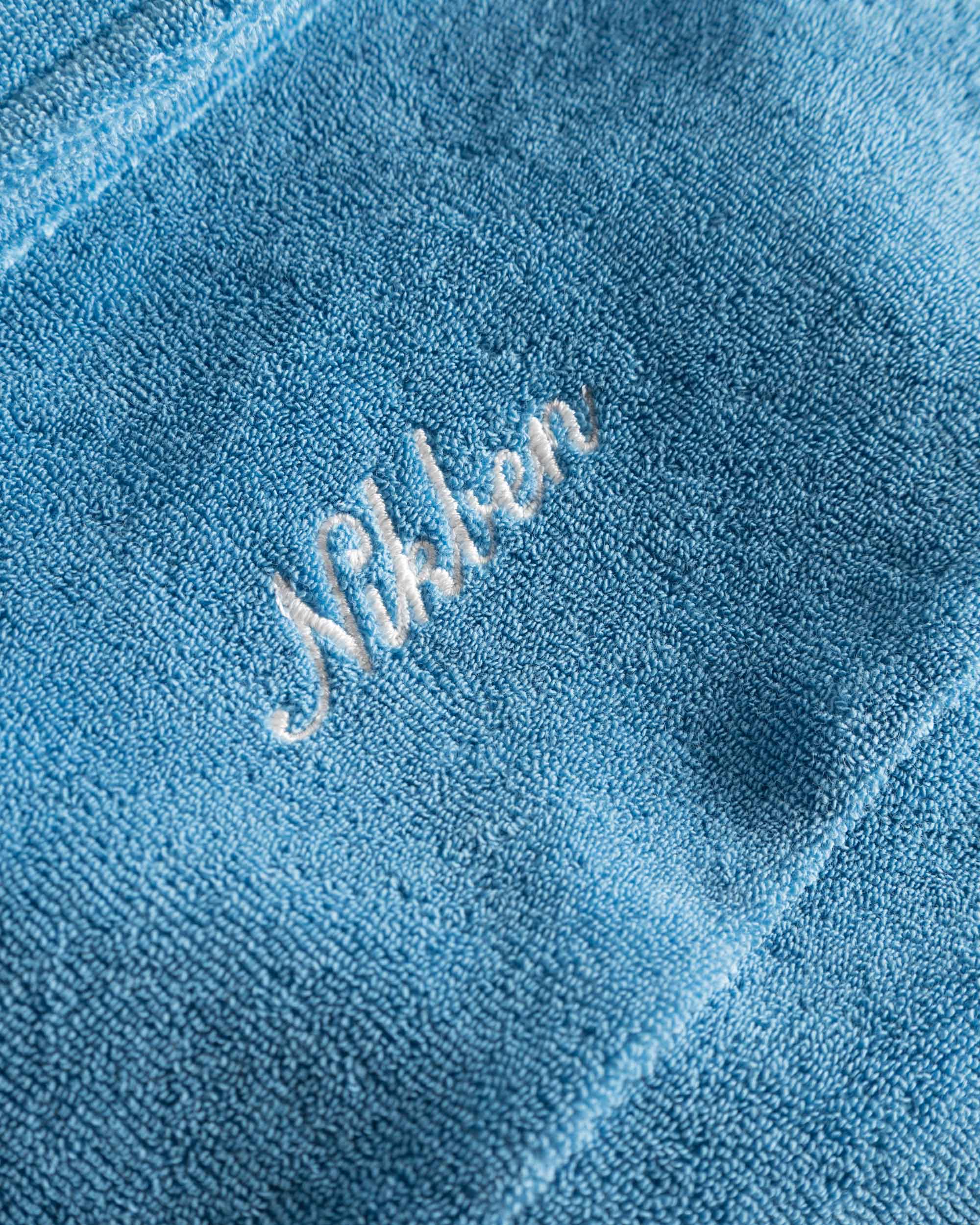 Close up of embroidered script on a white and sky blue short sleeve shirt