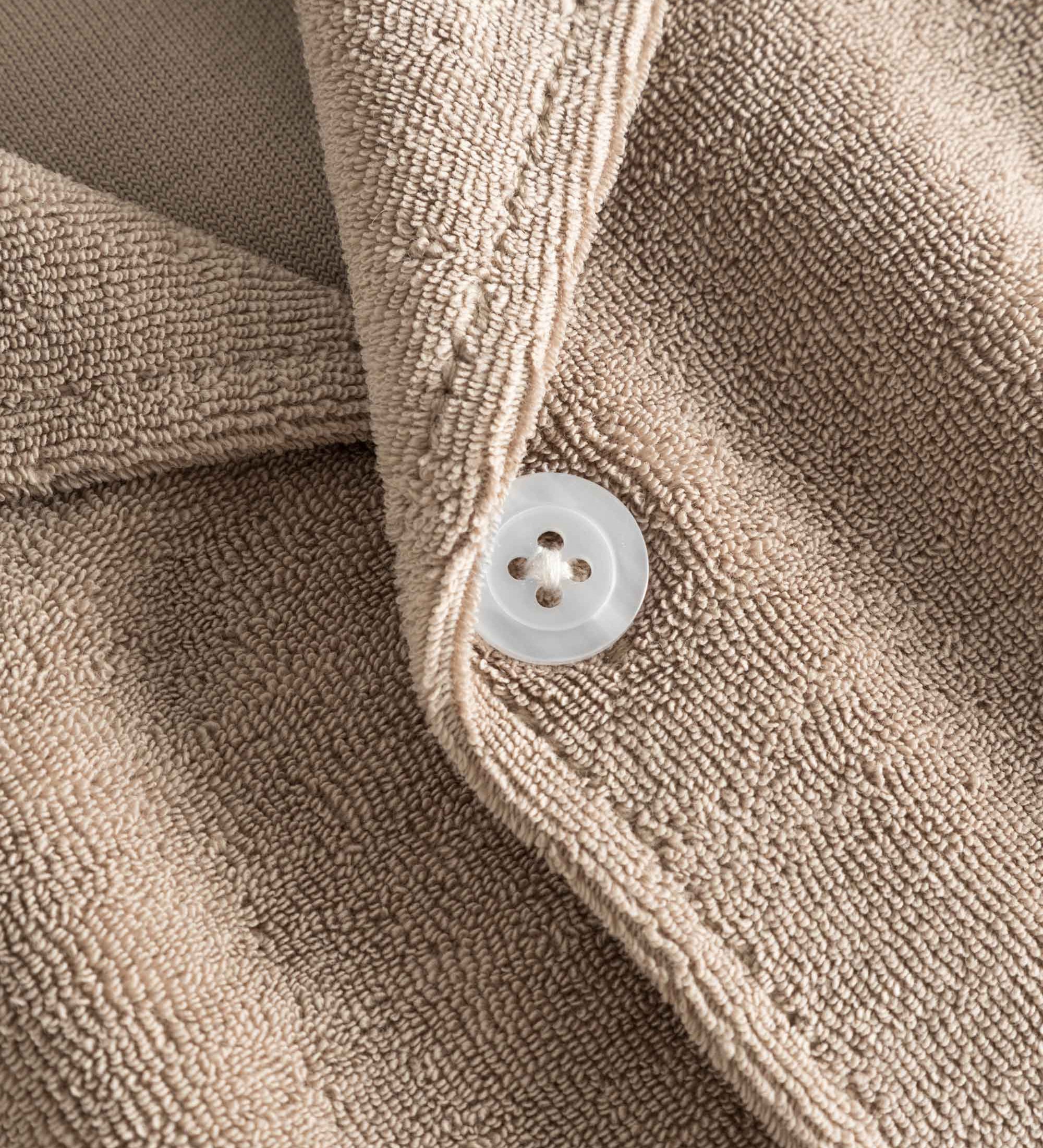 Close up on white pearl button on a light brown, short sleeve, cropped shirt