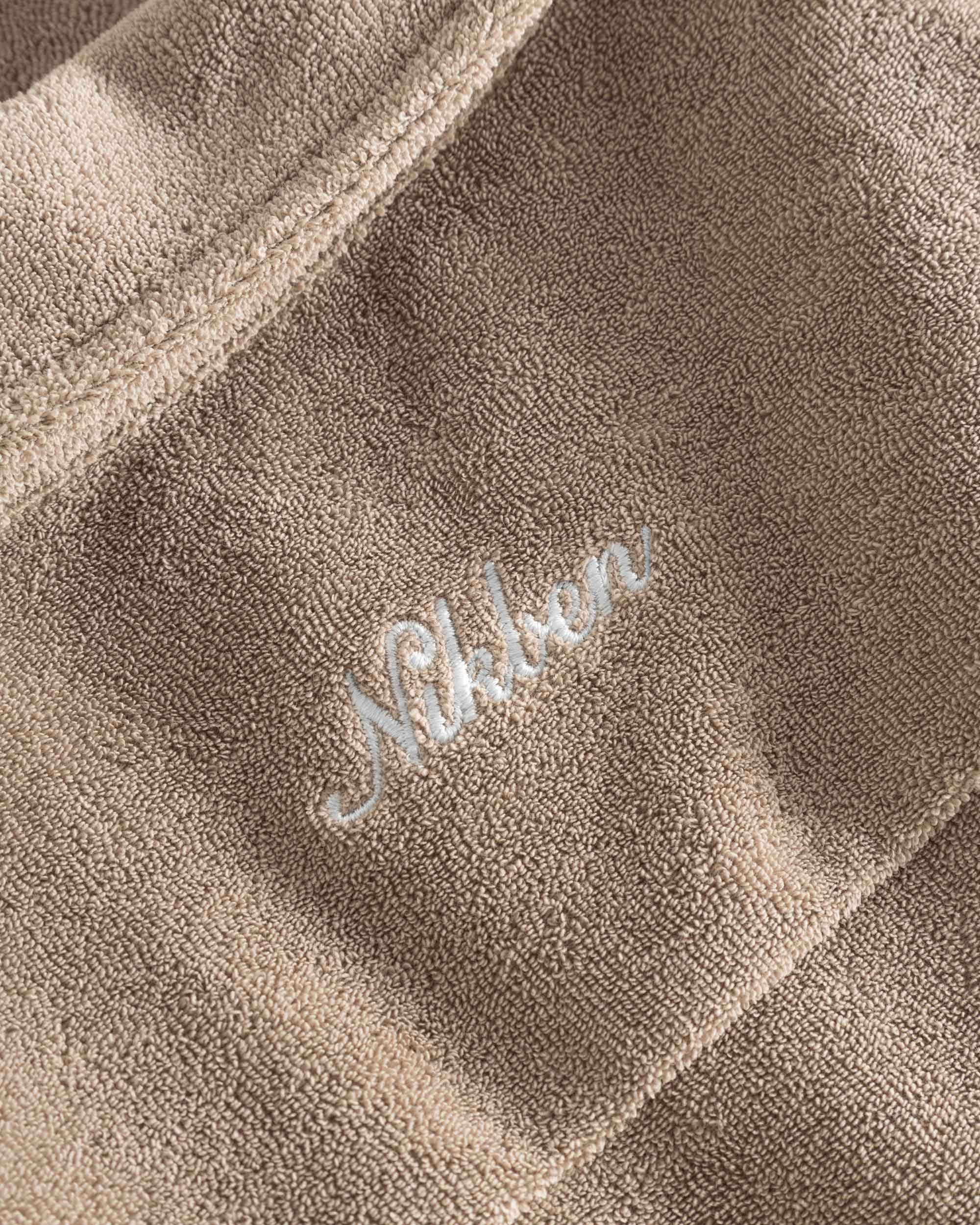 Close up on embroidered logo on a light brown, short sleeve, cropped shirt