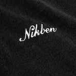 Close up view of a white embroidered "nikben" logo on a black hoodie.