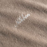 Close up of a white embroidered "Nikben" logo on a beige Terry hoodie.