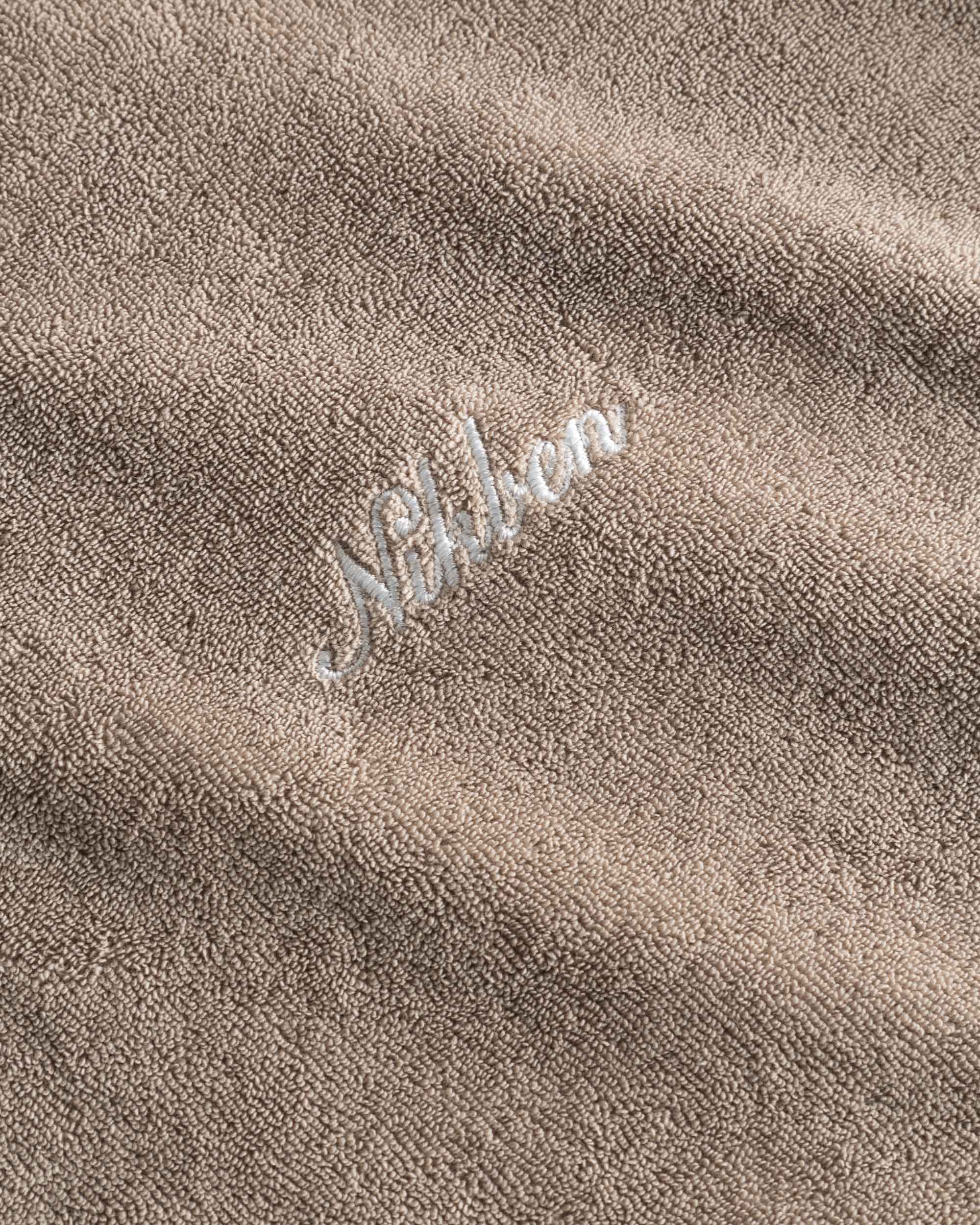 Close up of a white embroidered "Nikben" logo on a beige Terry hoodie.