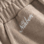 Close up of embroidered logo on light brown low cut shorts in terry toweling fabric