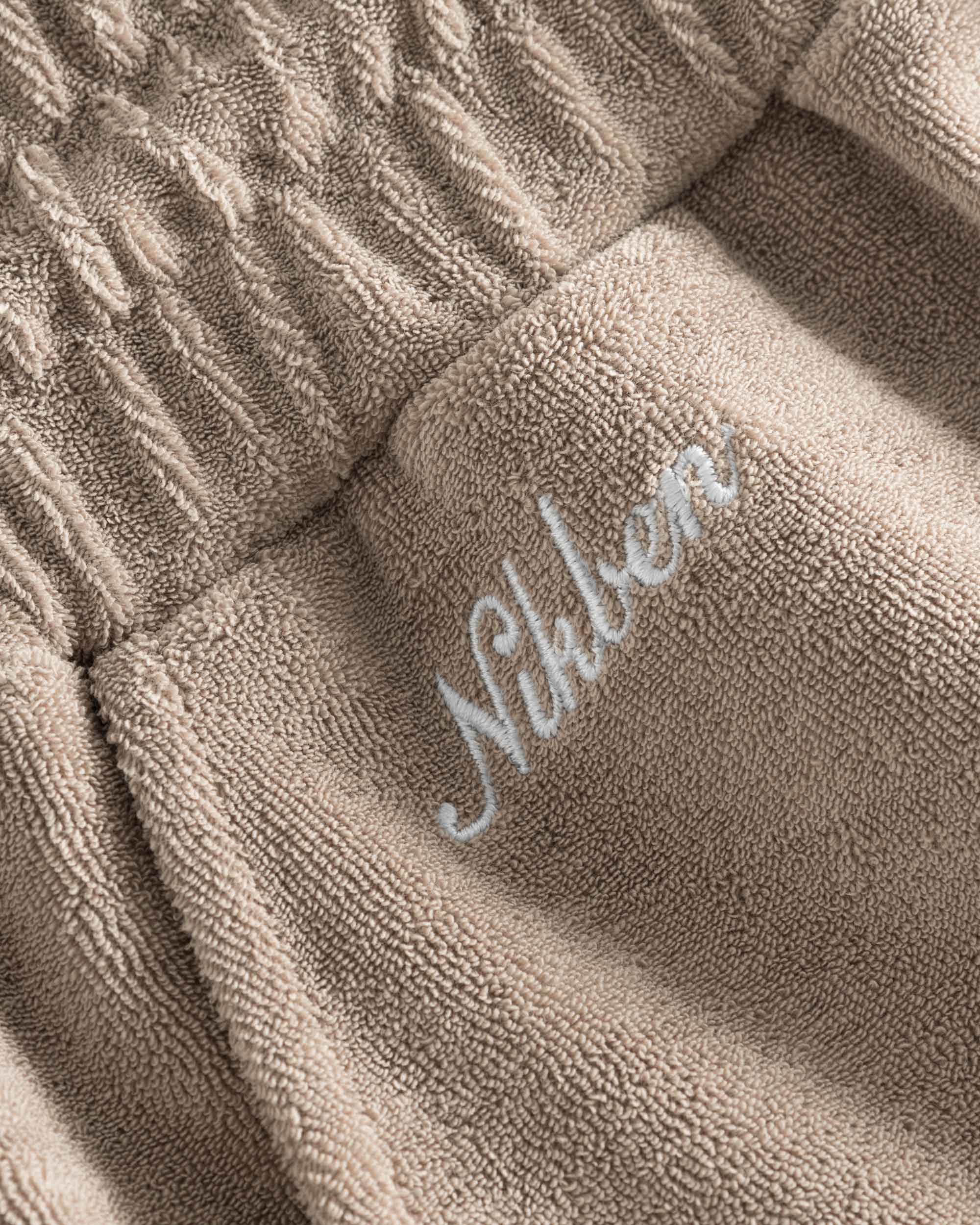Close up of embroidered logo on light brown low cut shorts in terry toweling fabric