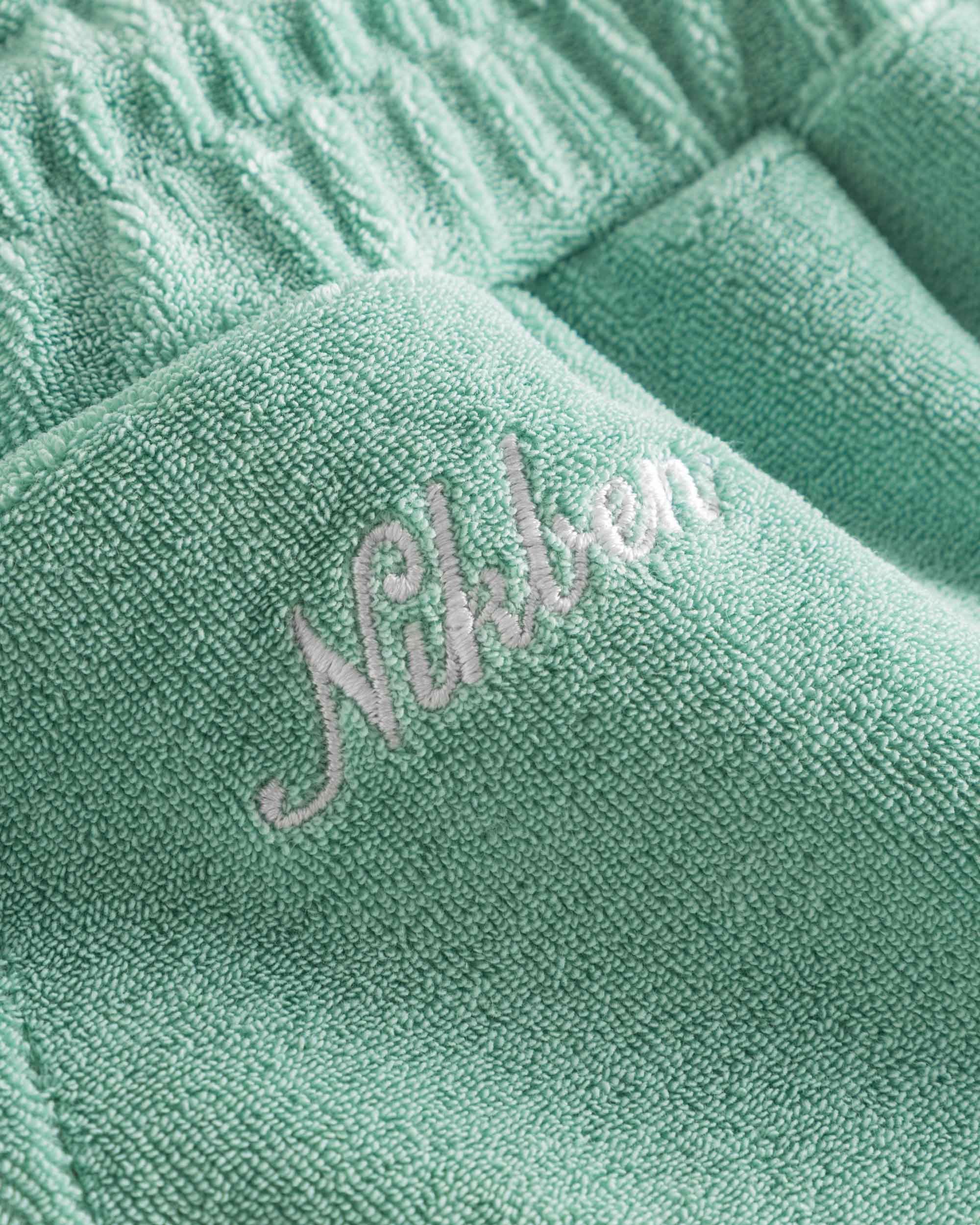 Close up of embroidered logo on grey-green low cut shorts in terry toweling fabric