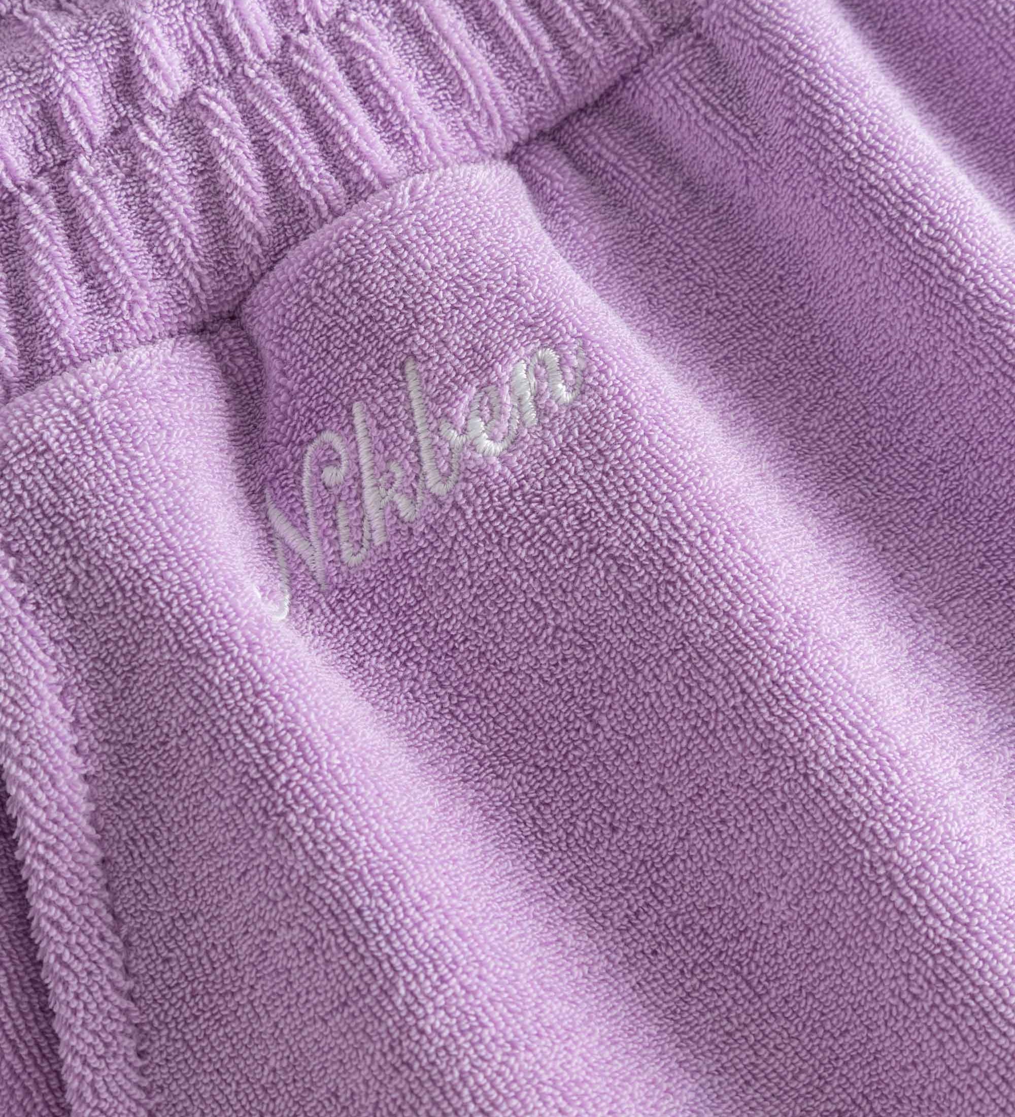 Close up of embroidered logo on purple low cut shorts in terry toweling fabric