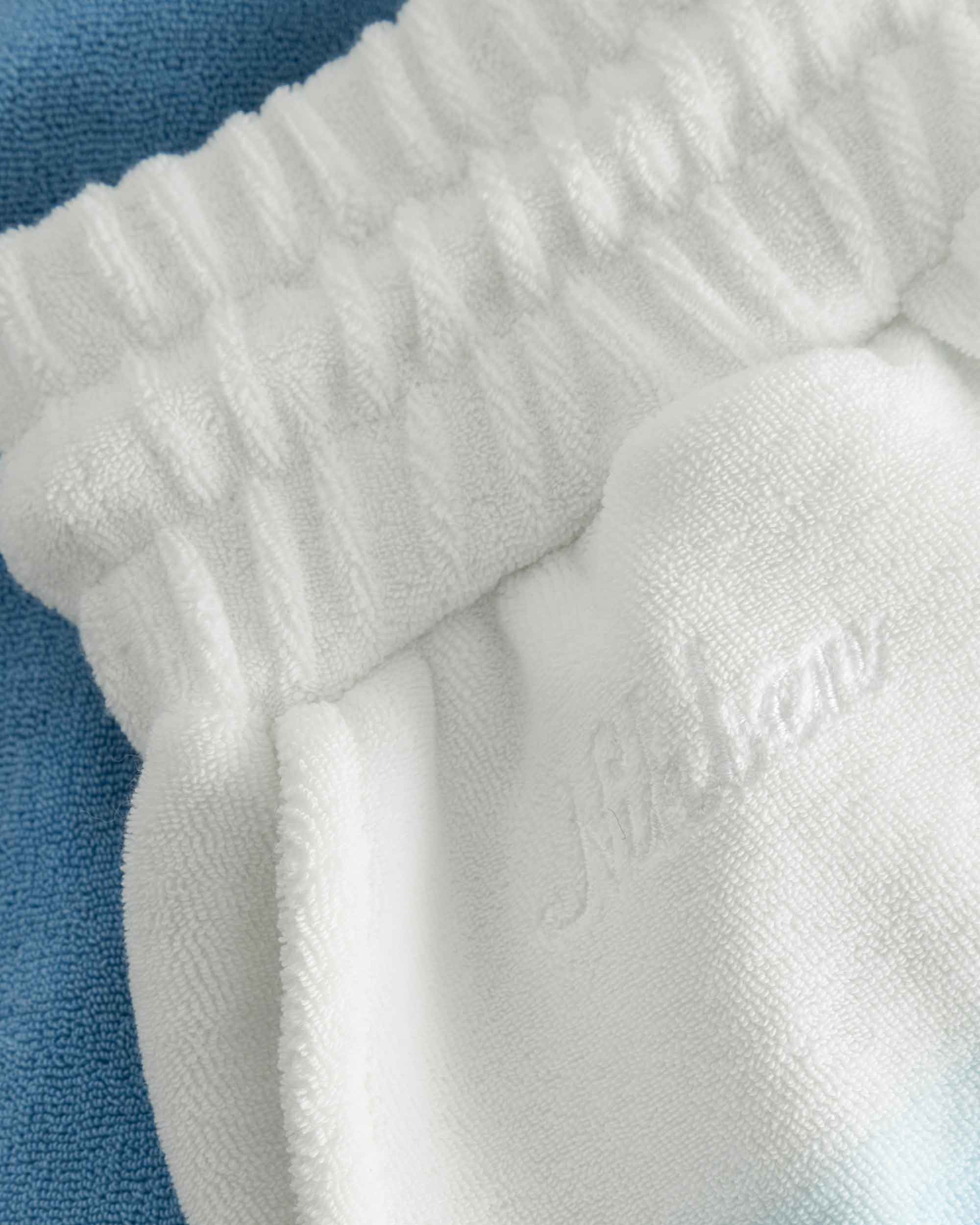 Close up on embroidered logo on white and sky blue low cut shorts in terry toweling fabric